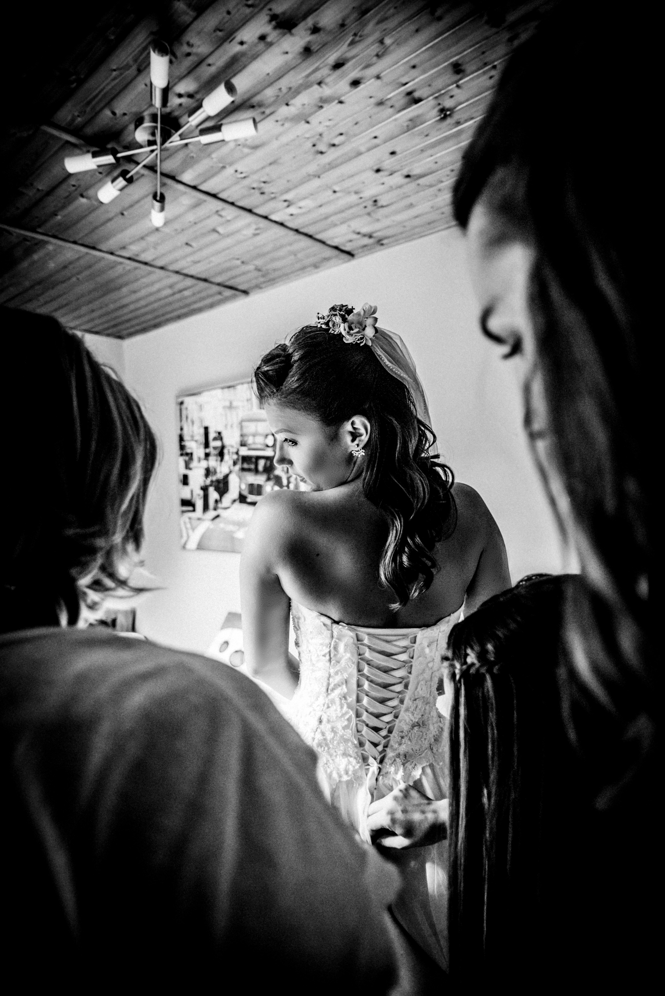 Bride looking over her shoulder while family finish lacing her wedding gown in black and white.
