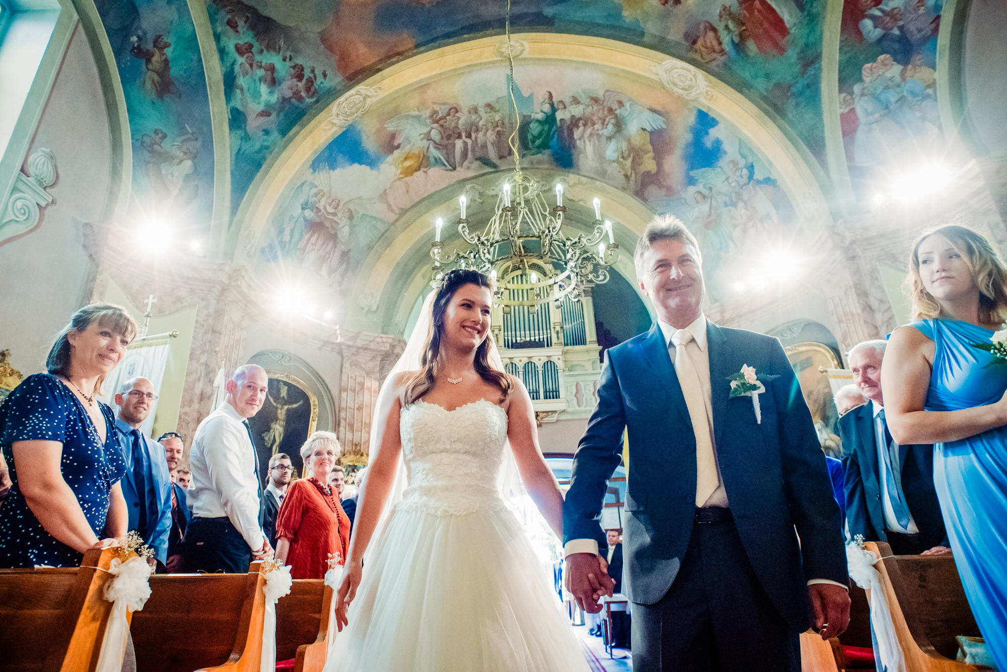 Bride entering a painted church with her father during a summer wedding ceremony in Hungary.