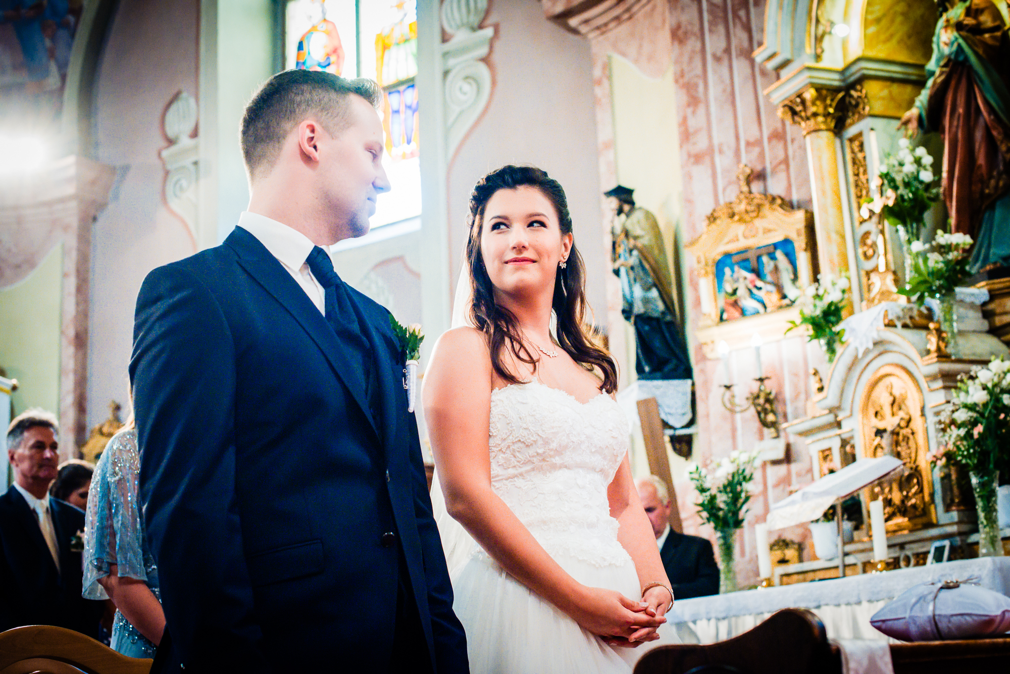 Bride and groom exchanging glances during their church wedding ceremony beneath ornate frescoes.