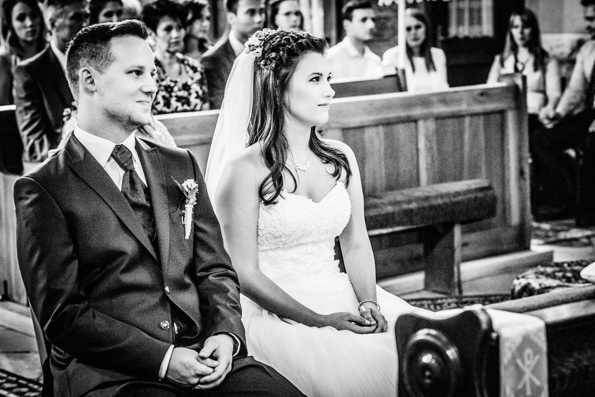 Bride and groom seated during a Catholic wedding ceremony inside a historic Hungarian church.