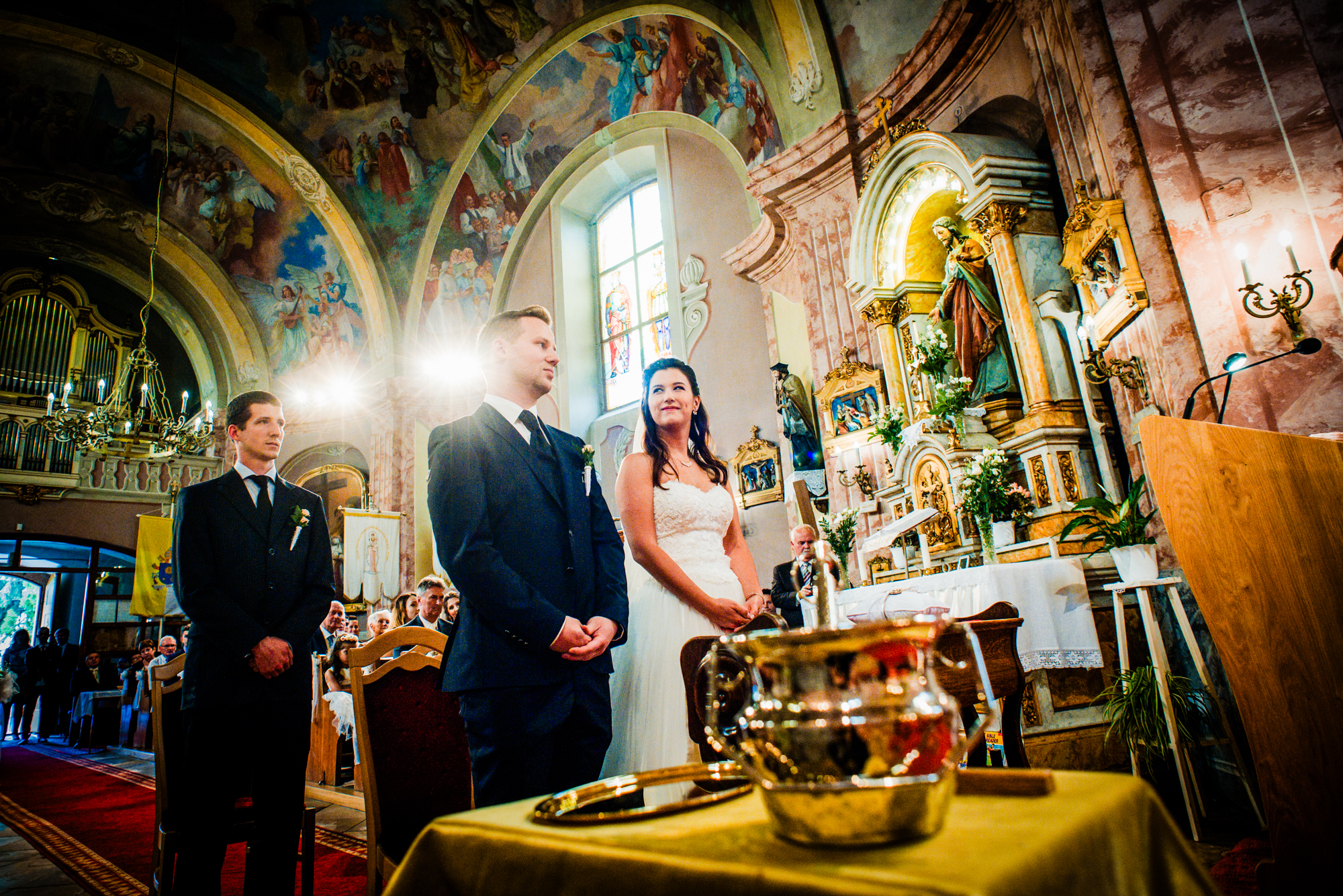 Wide view of a church wedding ceremony with ornate frescoes and dramatic light in Hungary.