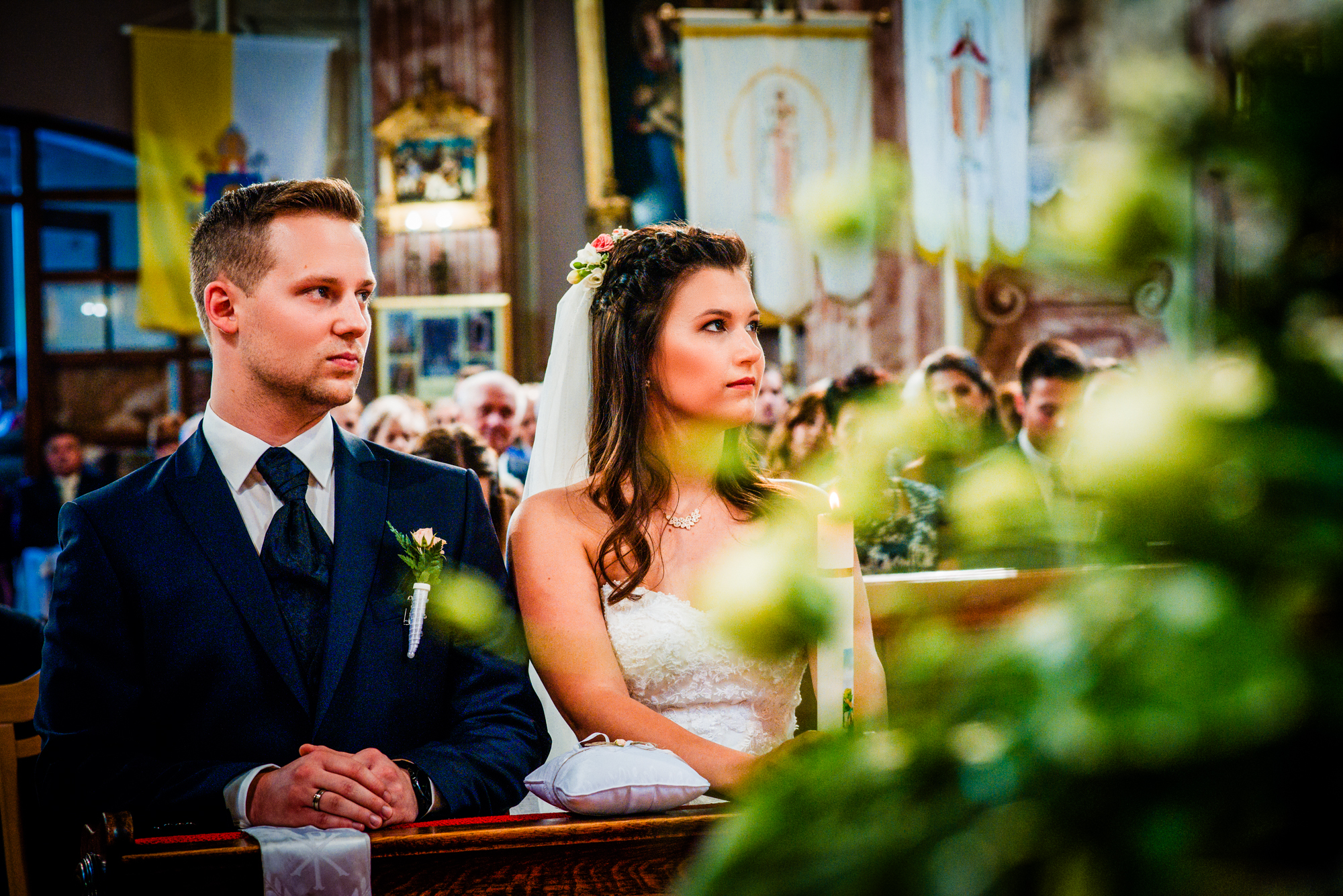 Bride and groom seated together during the wedding ceremony with soft greenery framing the foreground.