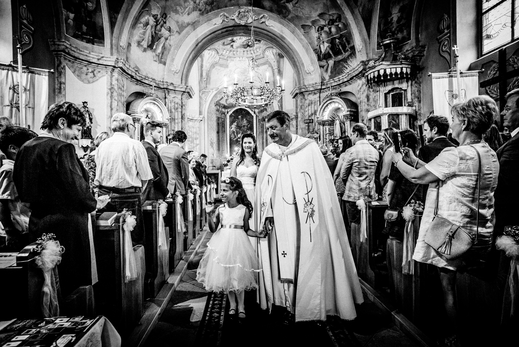 Priest and flower girl walking down the aisle after a church wedding ceremony in Hungary.