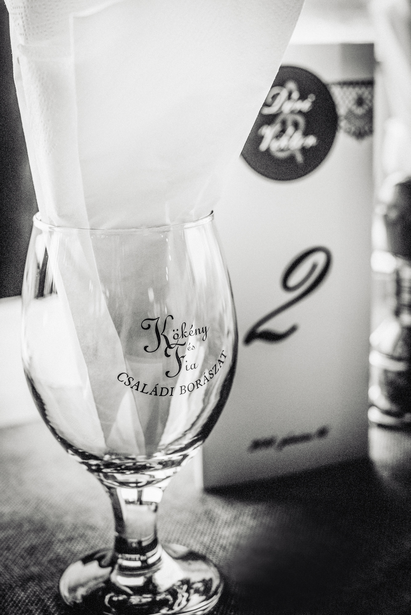 Personalised wedding wine glass beside reception menu at rustic vineyard wedding in Hungary.