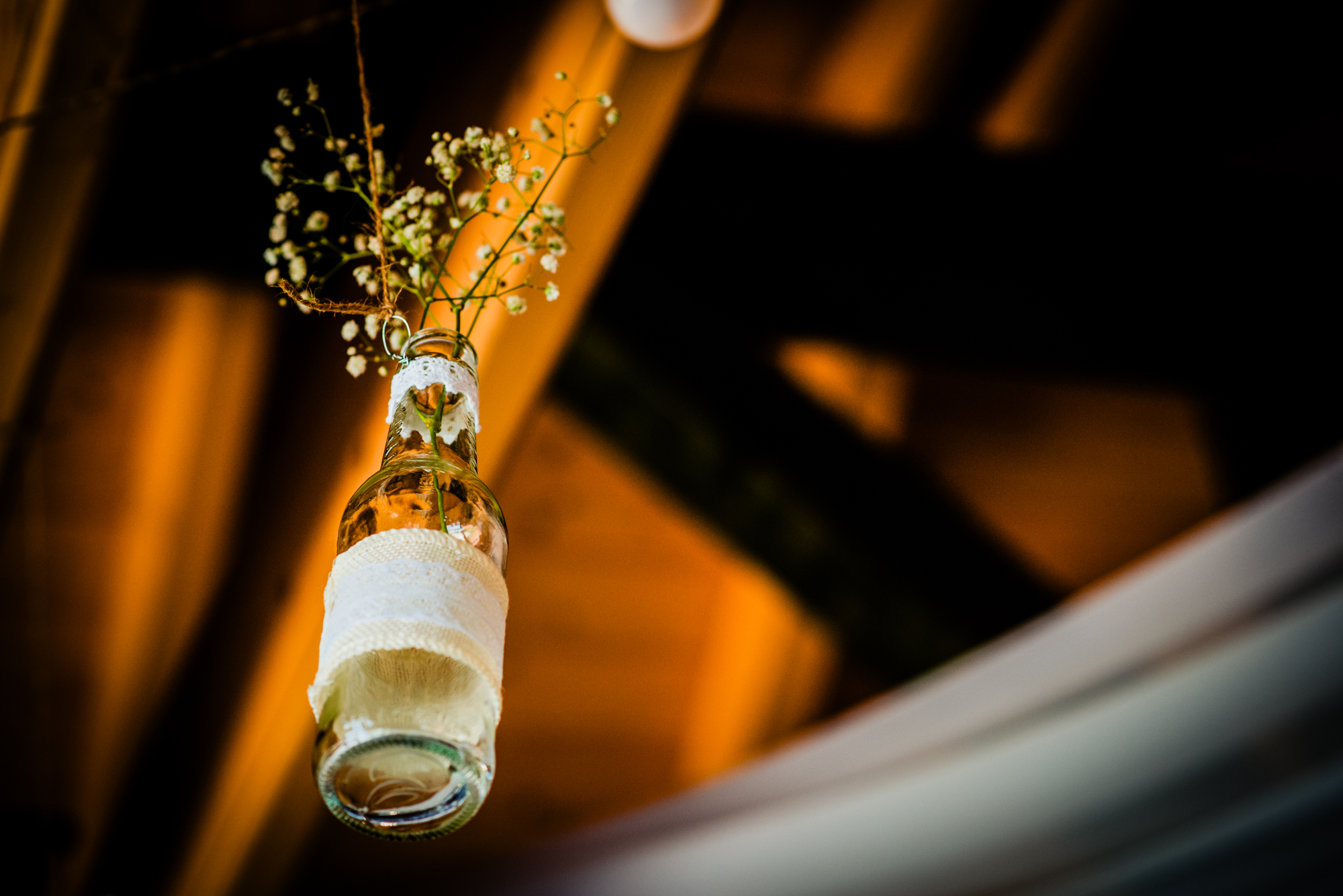 Hanging glass bottle decoration with baby’s breath flowers at rustic wedding reception venue.