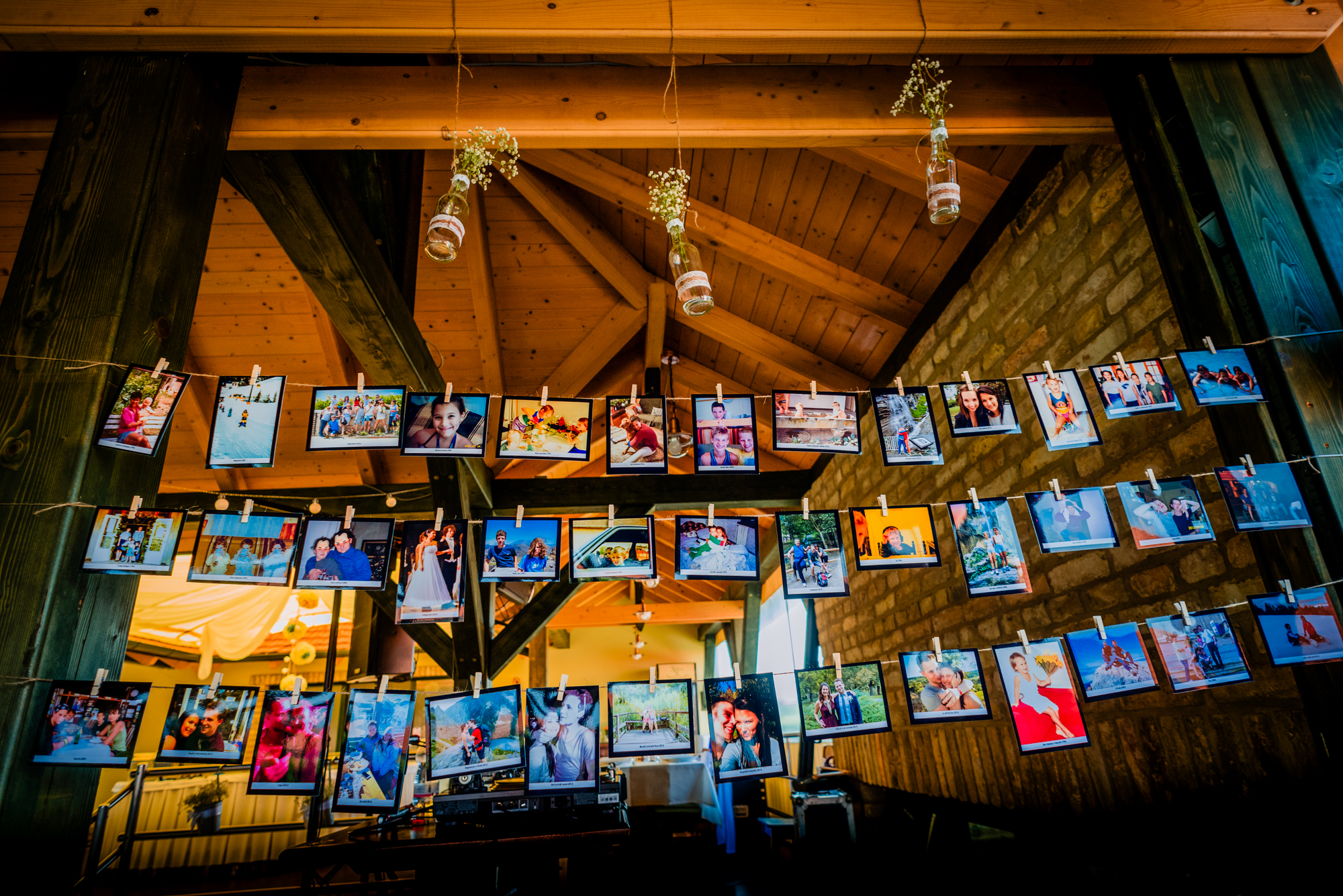 Childhood and family photographs hanging as wedding décor inside a rustic wooden reception space.