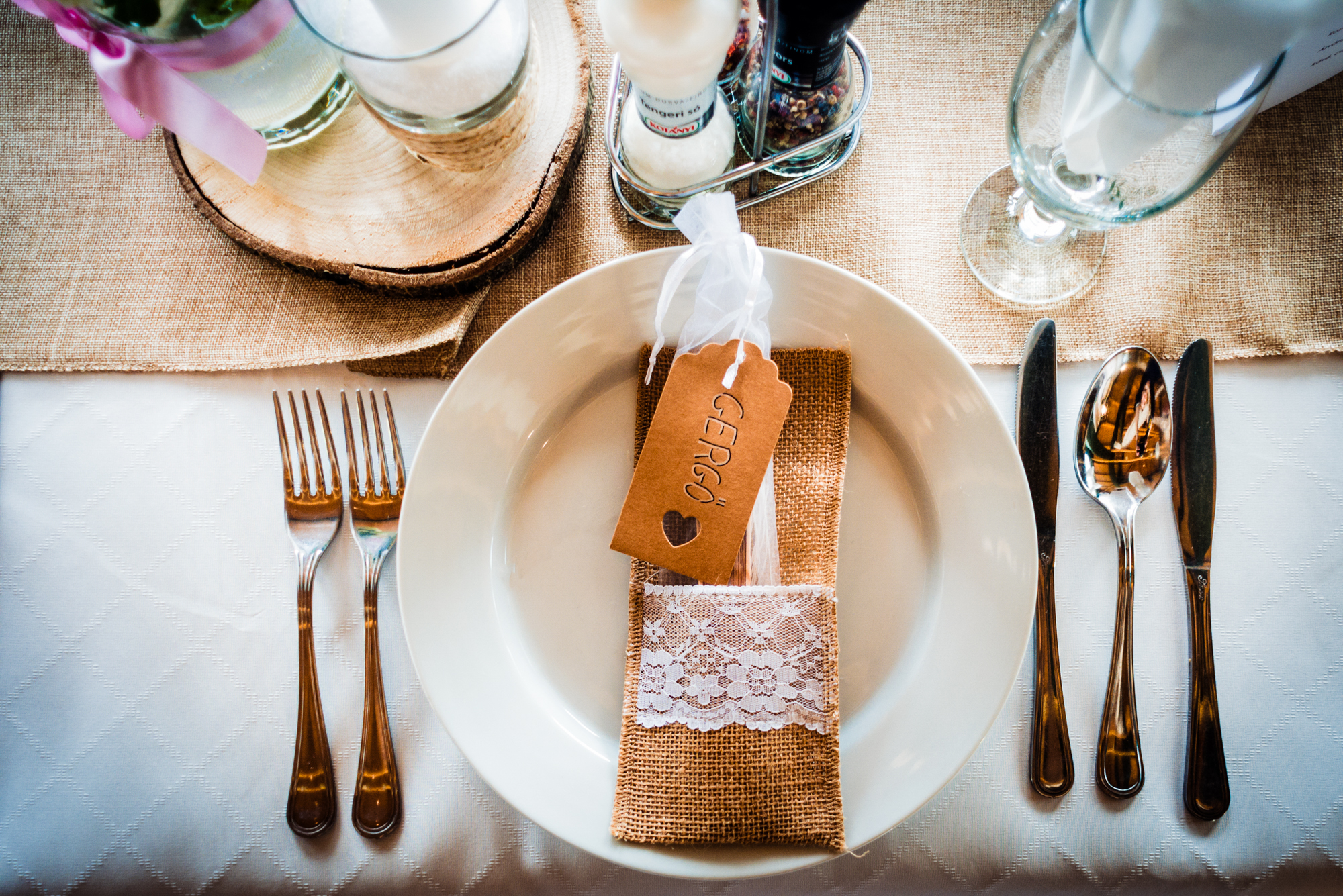 Rustic wedding place setting with burlap napkin holder and handwritten guest name tag.