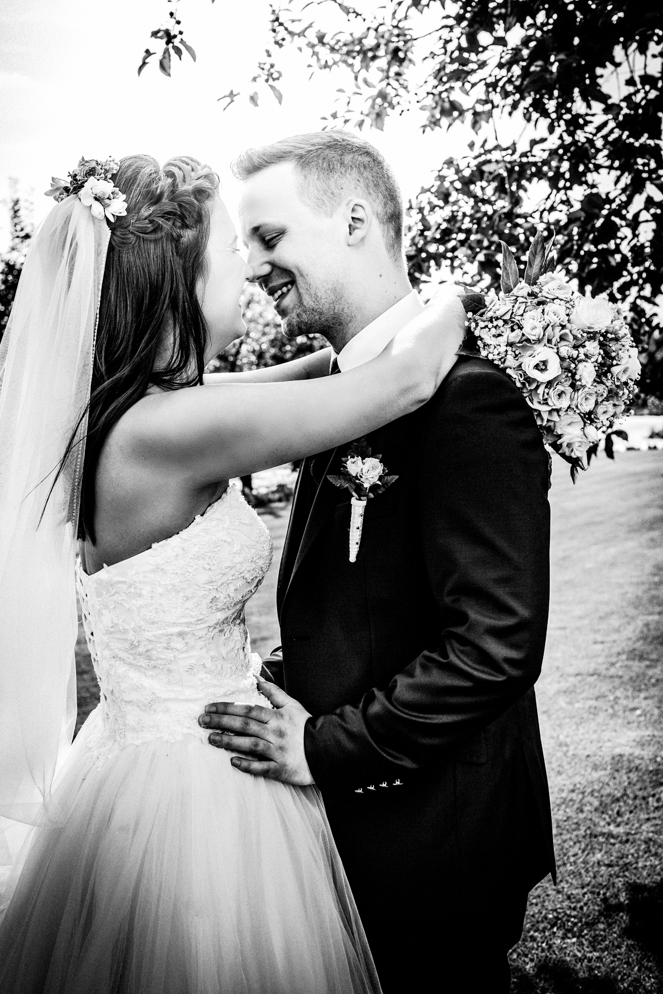 Black and white portrait of bride and groom smiling together beneath trees at vineyard wedding.