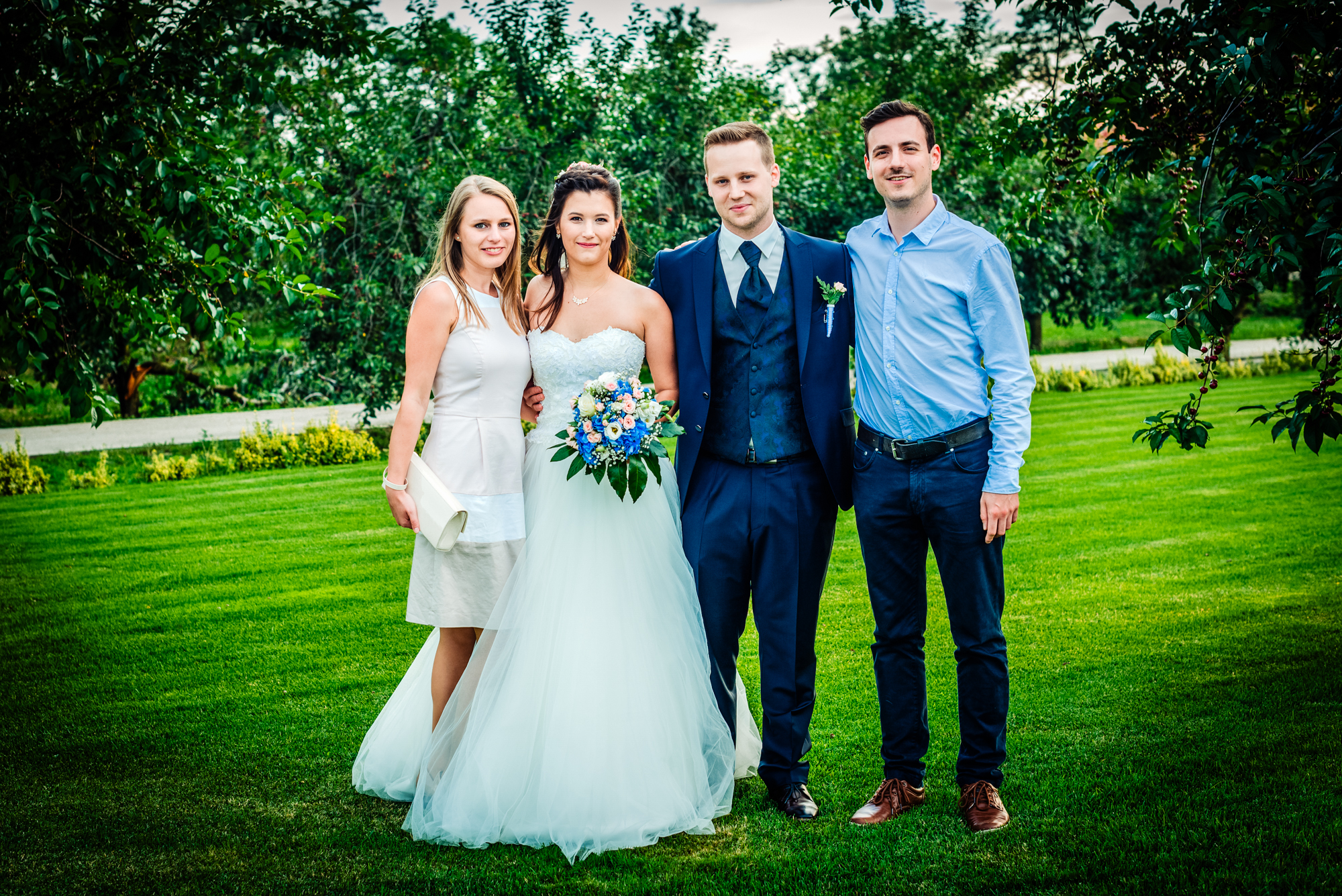 Bride and groom posing with wedding guests on green lawn during vineyard wedding celebration.