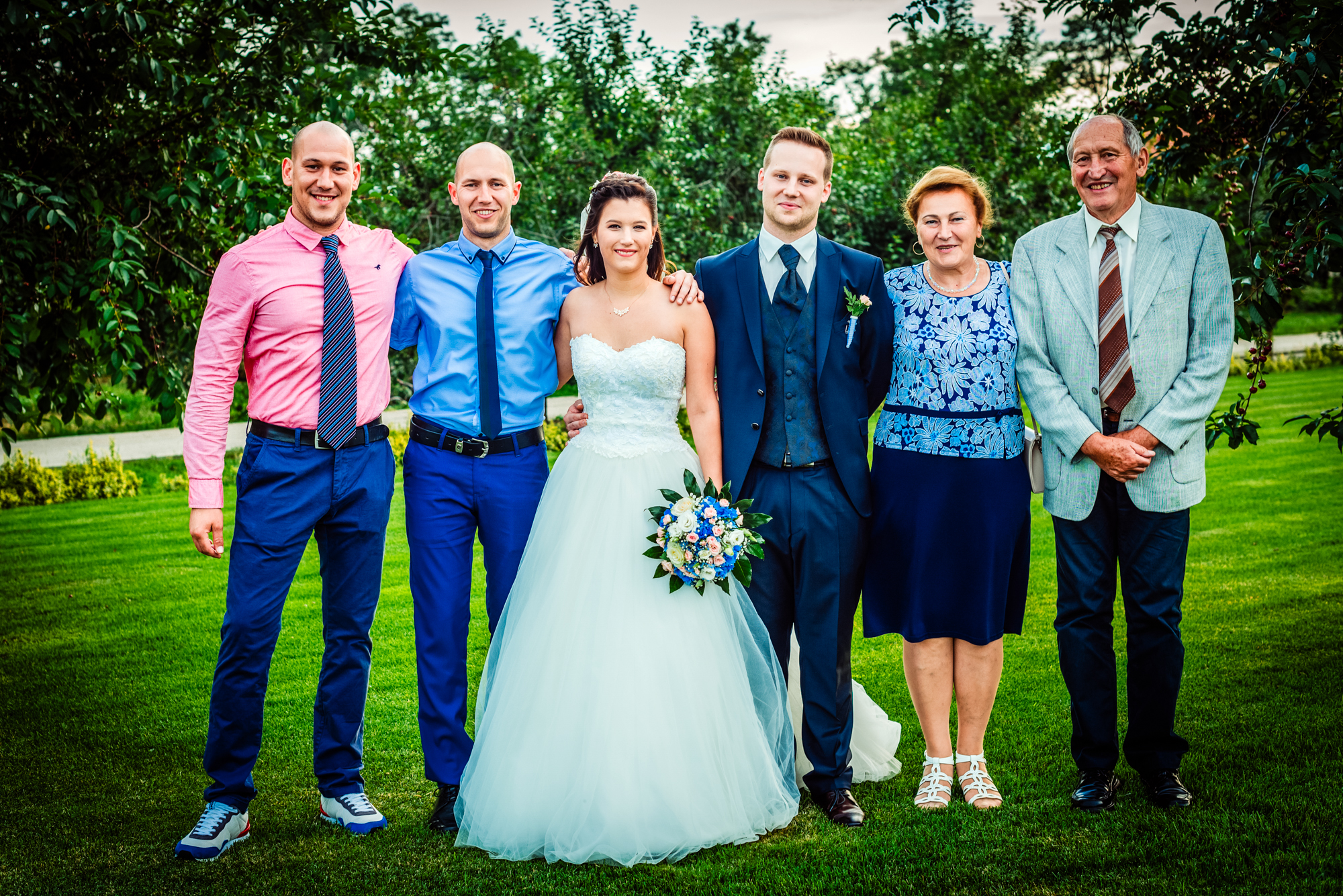 Bride and groom posing with family members outdoors during summer wedding in Hungary.