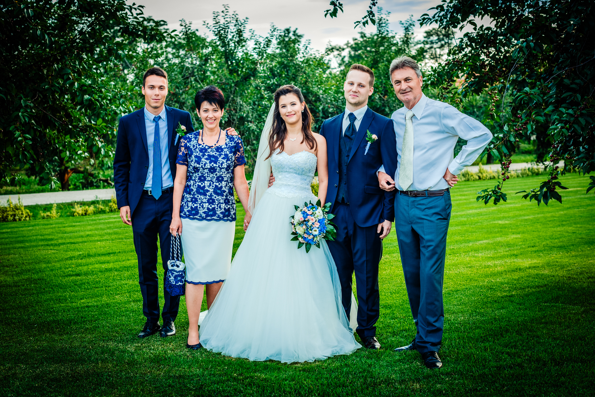 Bride and groom posing with parents and brother on vineyard lawn during outdoor wedding portraits.