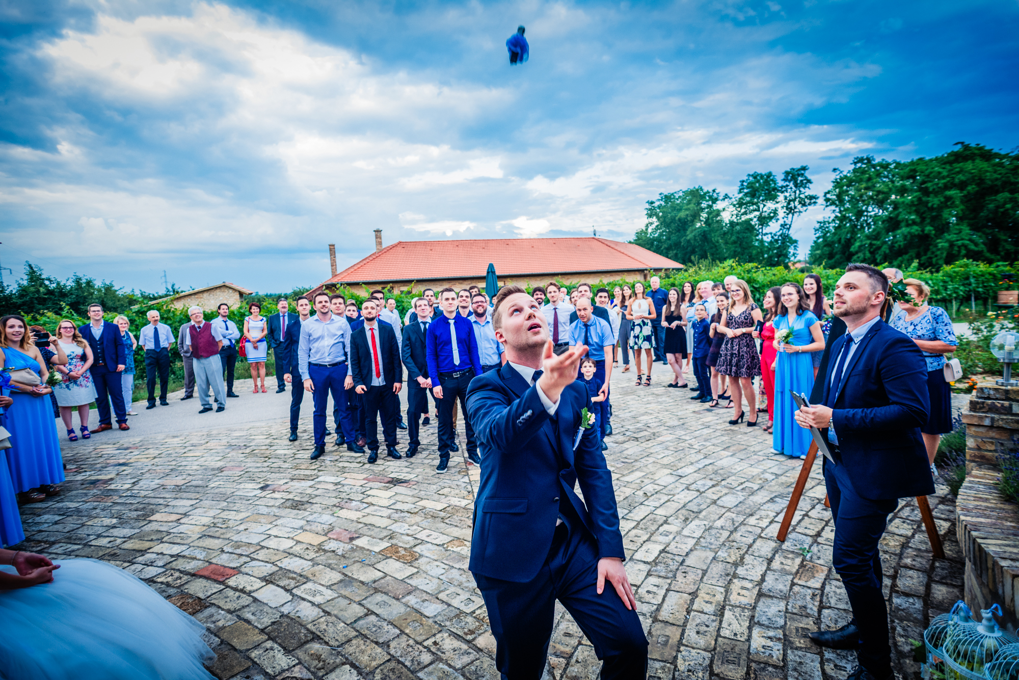 Groom preparing to catch garter during lively summer wedding reception in Hungary.