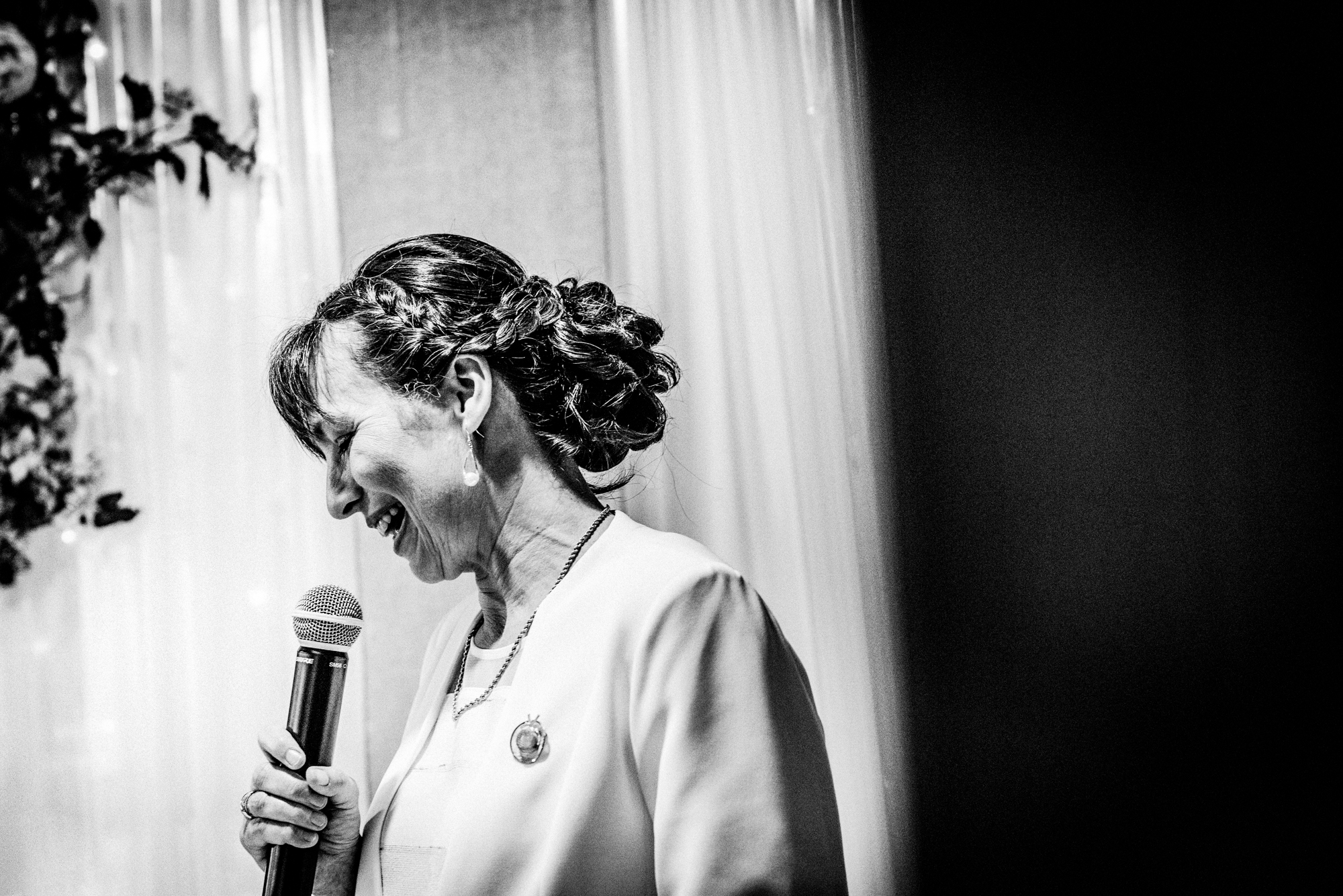 Mother of the groom giving an emotional wedding speech with microphone in black and white.