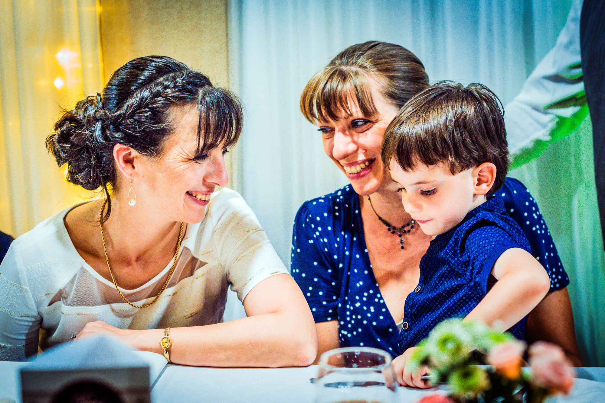 Mother and young boy smiling together at candlelit vineyard wedding reception in Hungary.