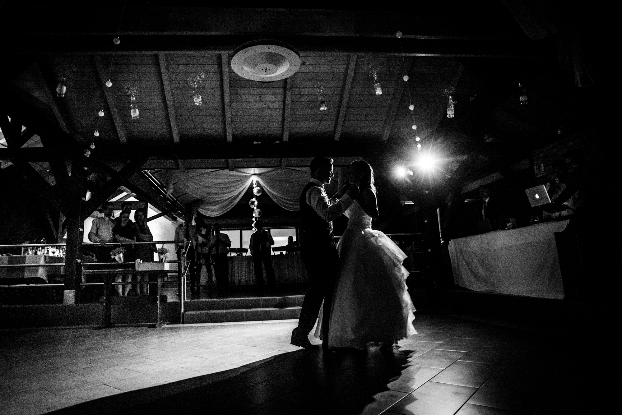 Bride and groom silhouetted during first dance inside rustic vineyard wedding venue at night.