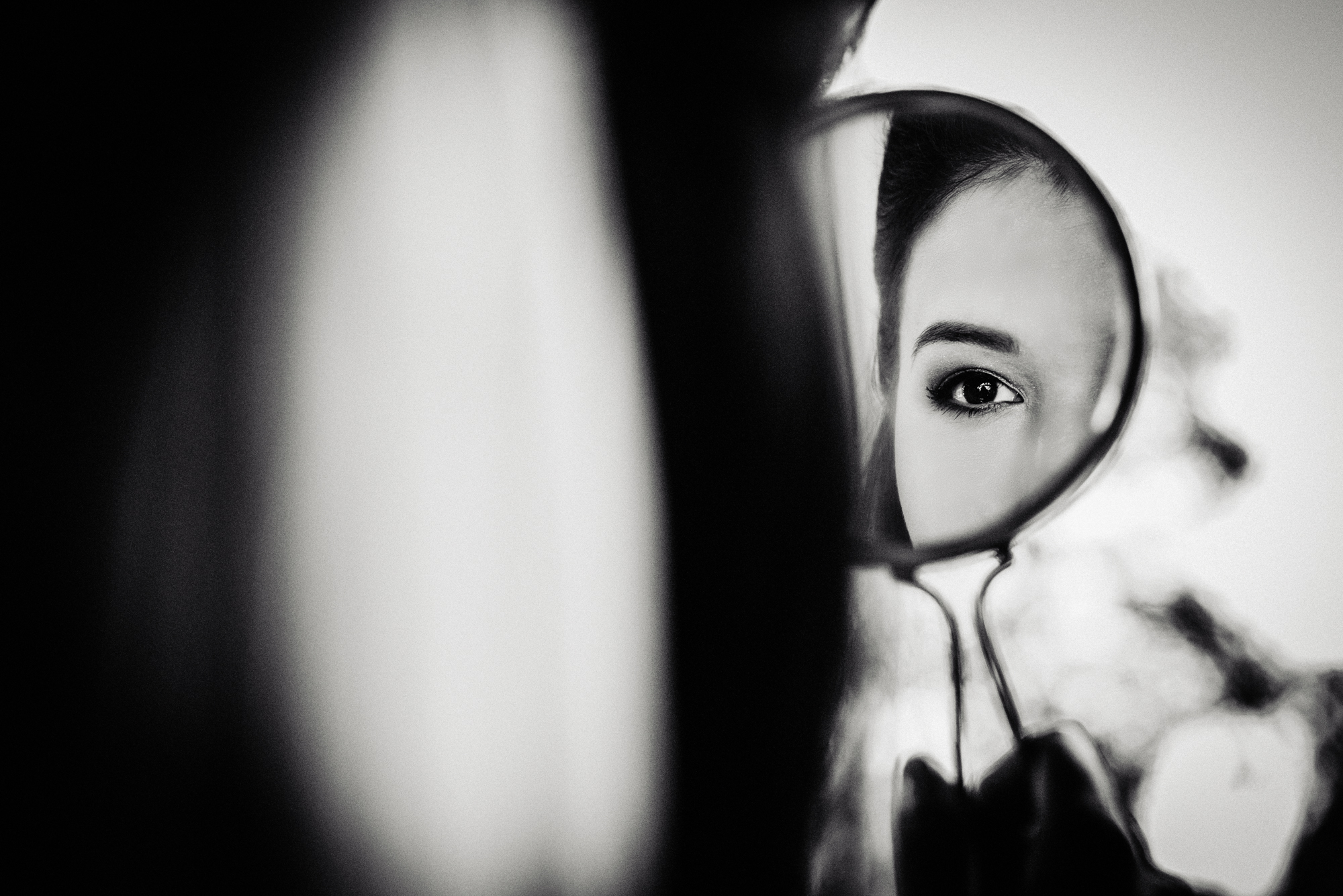 Black and white mirror reflection of the bride’s eye during quiet wedding morning preparations.