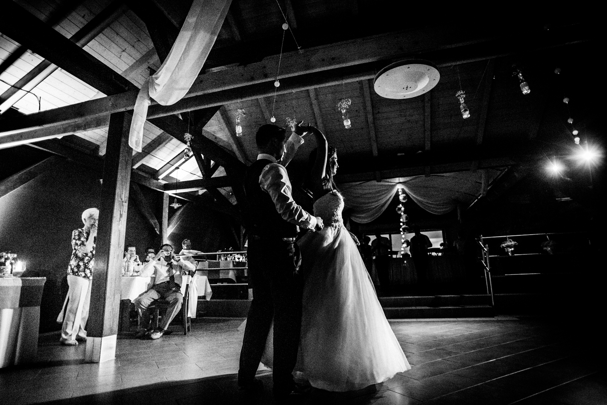 Bride twirling during romantic first dance inside dark wooden vineyard wedding venue.