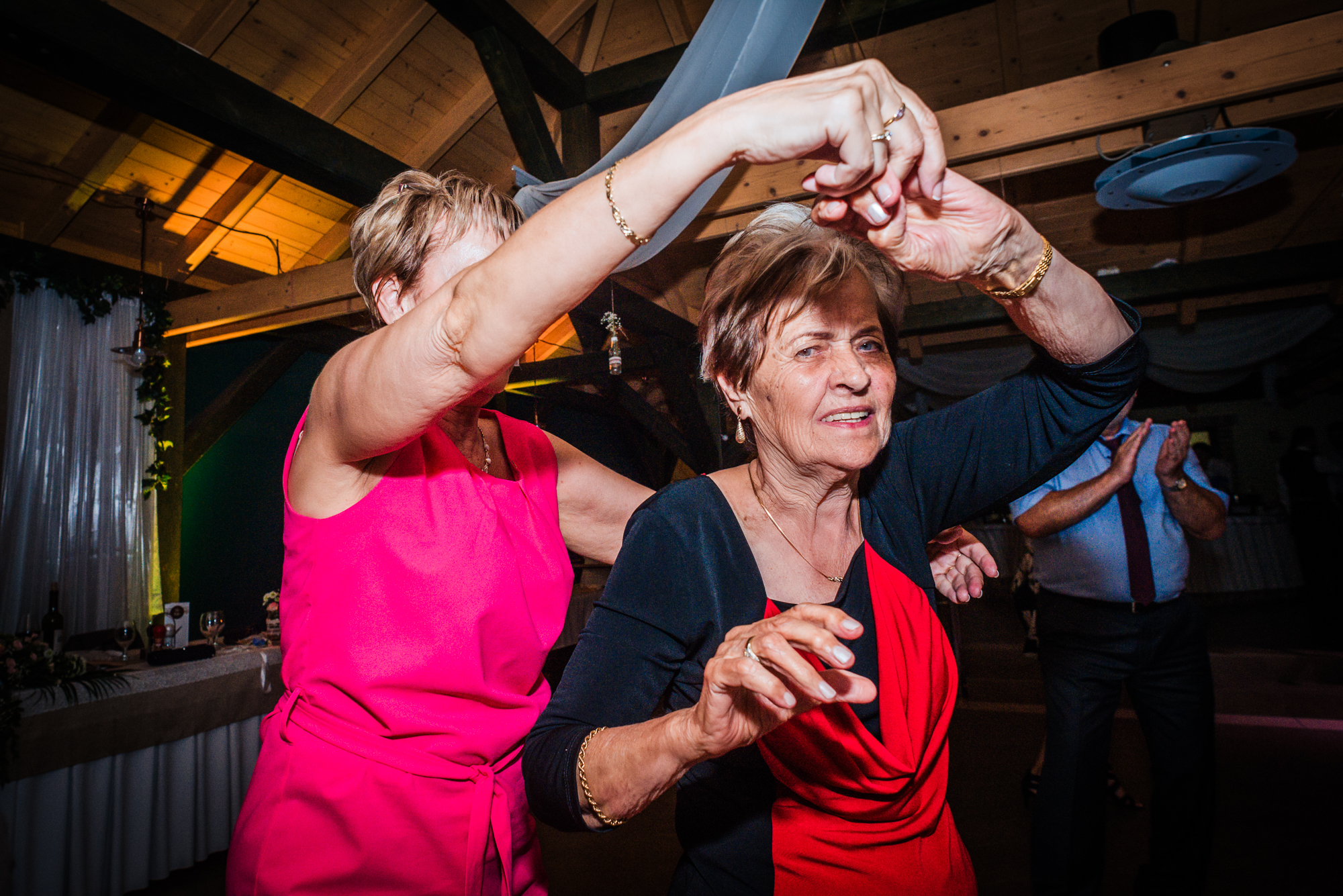Older wedding guests dancing together during lively evening reception in rustic wooden venue.