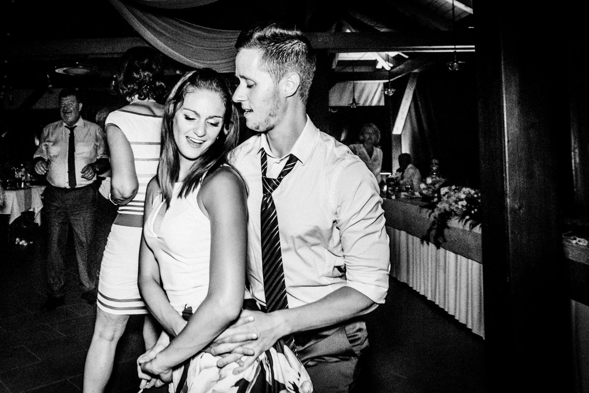 Young wedding guests dancing closely during crowded vineyard wedding party in black and white.