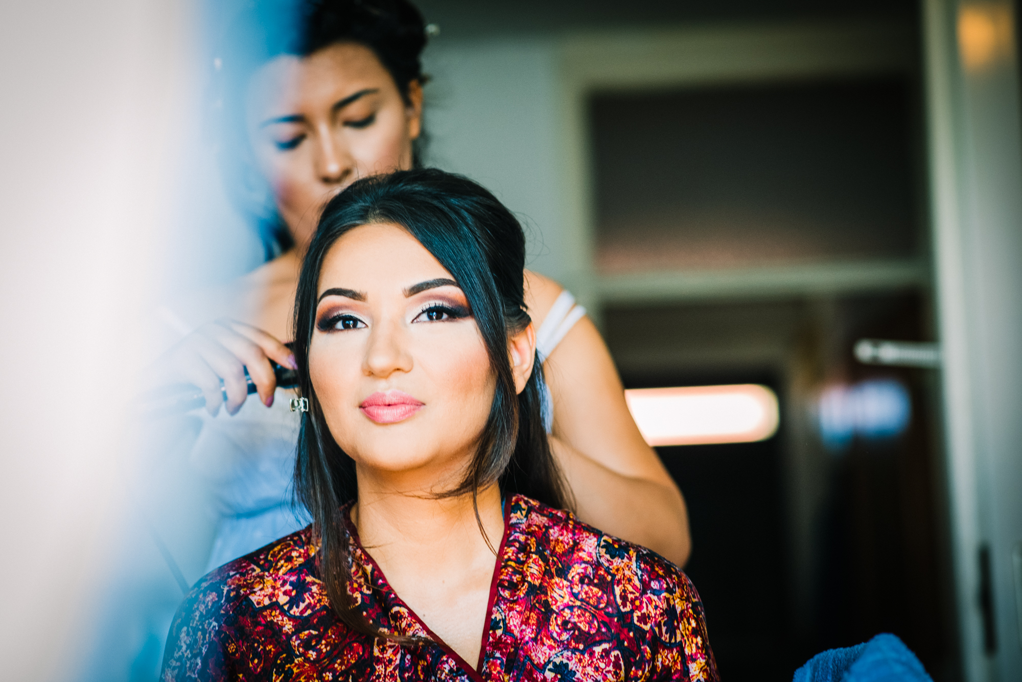 Bride having hair styled in soft window light, morning preparation in Budapest home.