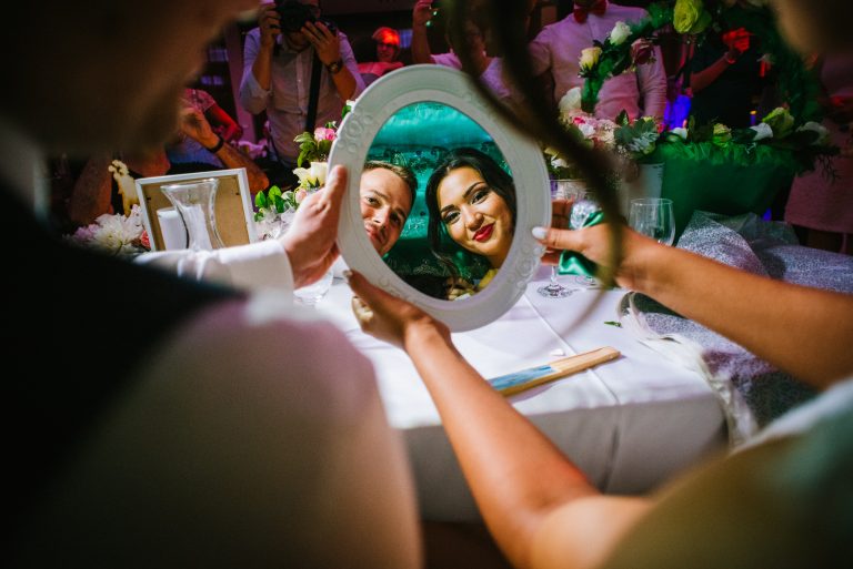 Couple reflected in small mirror held by them during first look afghan wedding reception moment.