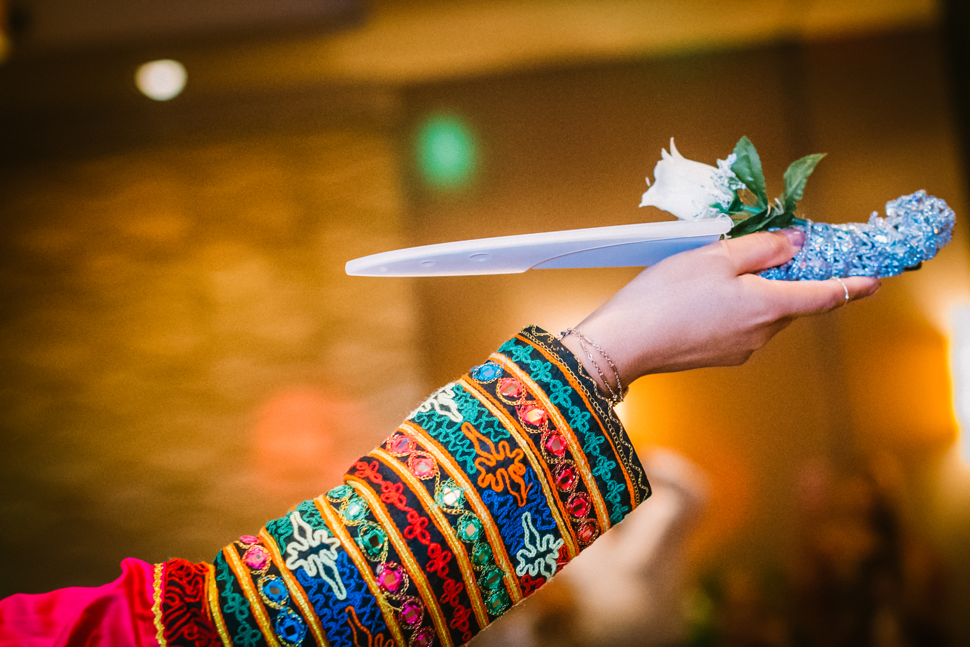 Close-up of embroidered traditional afghan sleeve holding ceremonial knife during cultural wedding ritual.