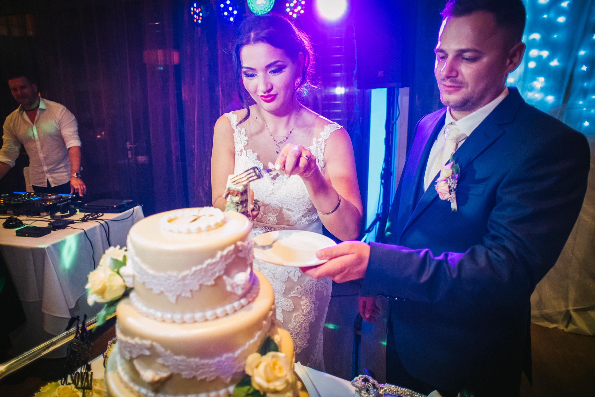 Couple cutting wedding cake together under vibrant reception lighting in Budapest.