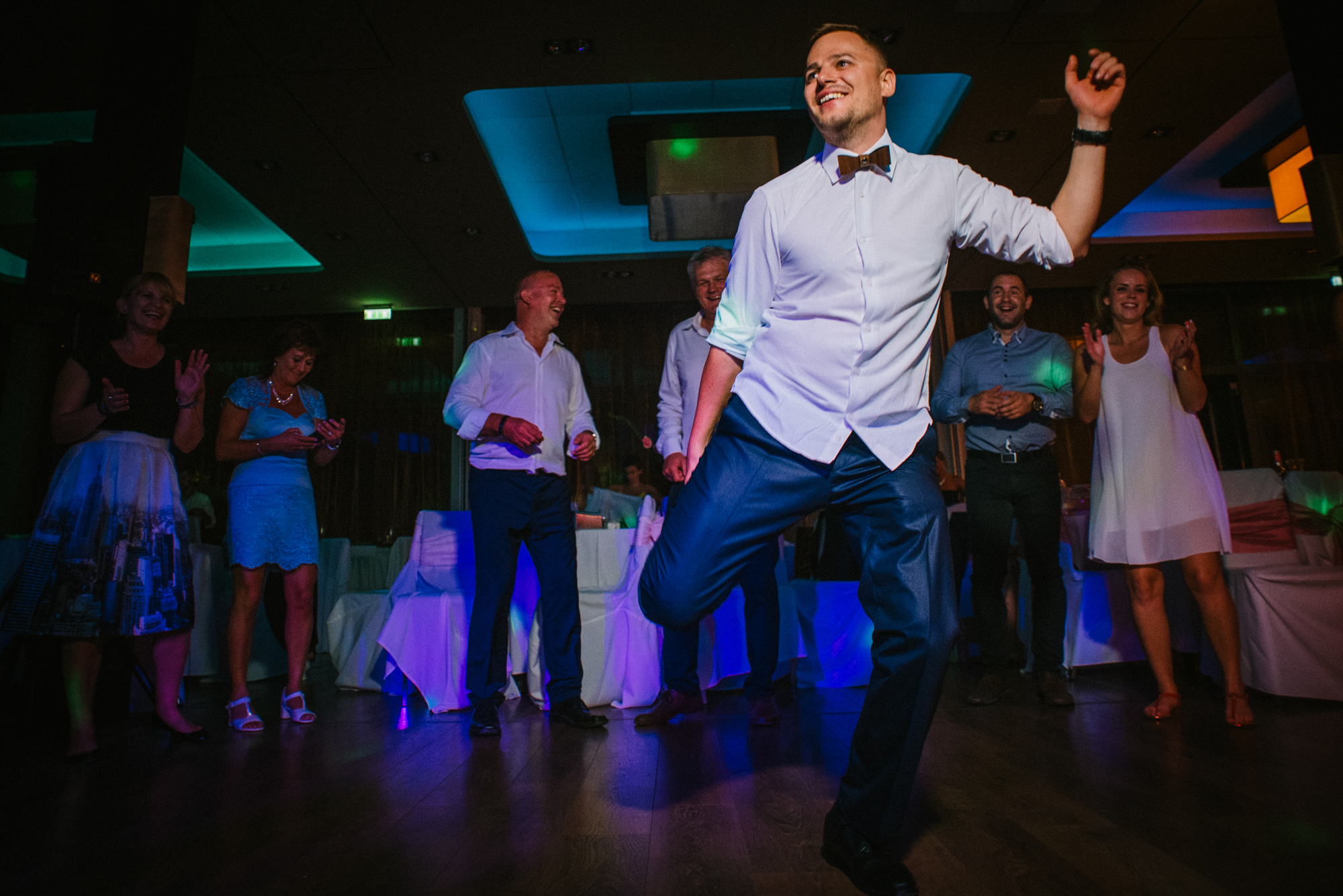 Dancing guests laughing under colourful party lights during Budapest wedding reception at Öbölház.