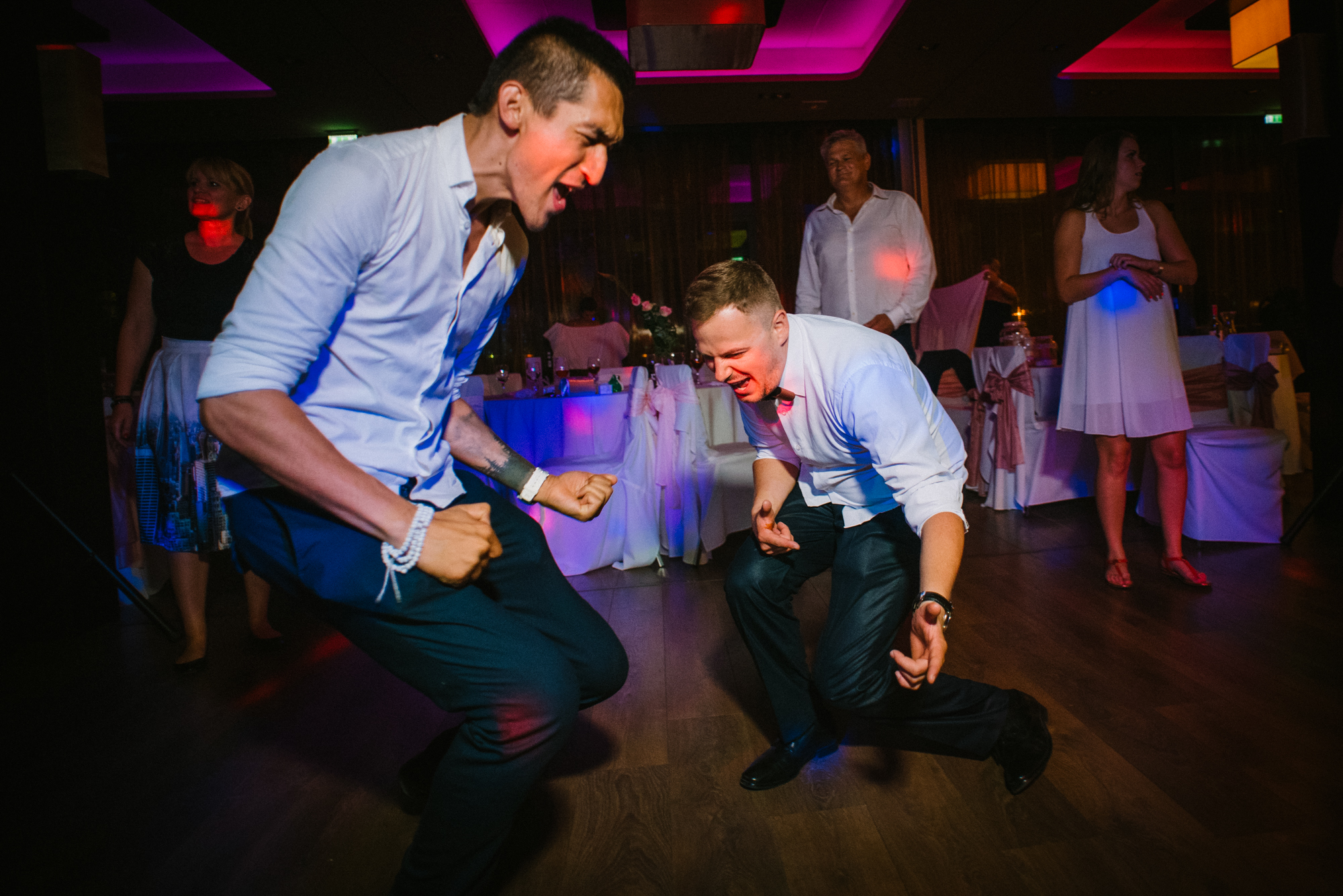 Two men dancing wildly and shouting with joy during lively wedding party in Budapest venue.