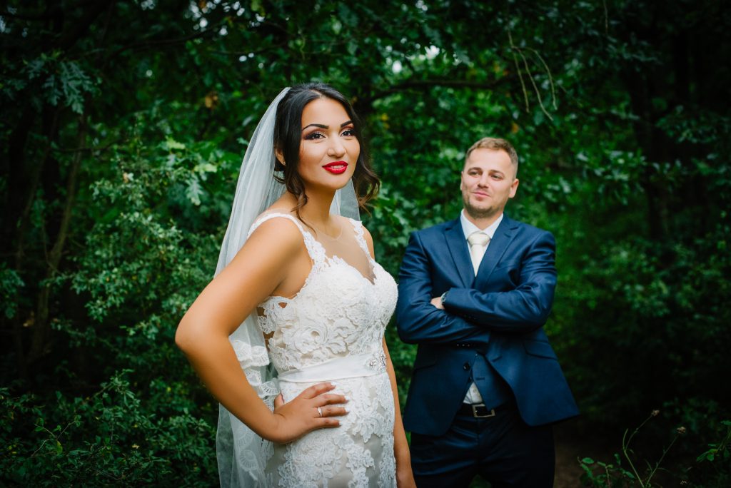 Bride posing confidently in forest while groom stands behind her during creative wedding portrait.