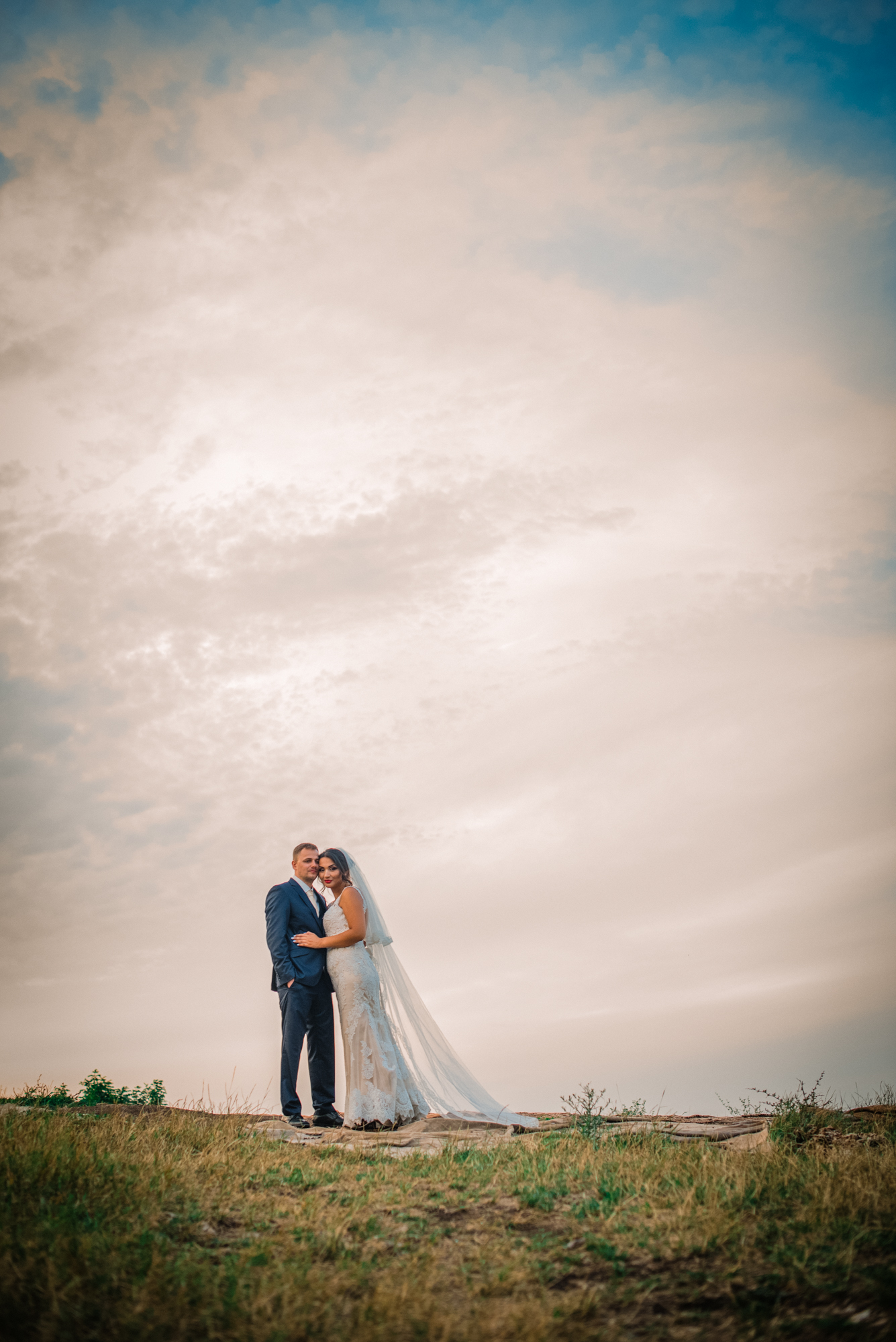 Bride and groom standing together on hill with dramatic sky during minimalist wedding portrait.