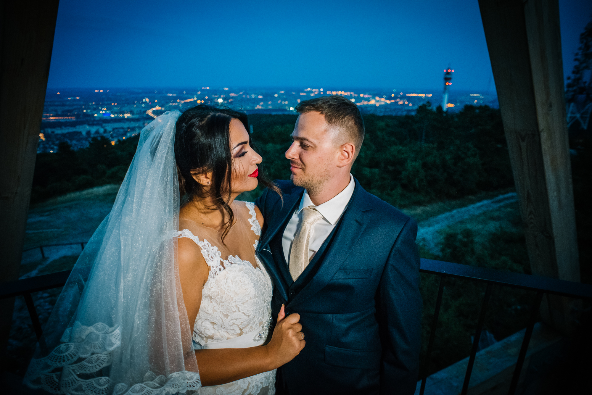 Bride and groom sharing quiet moment together during blue hour overlooking illuminated Budapest skyline.