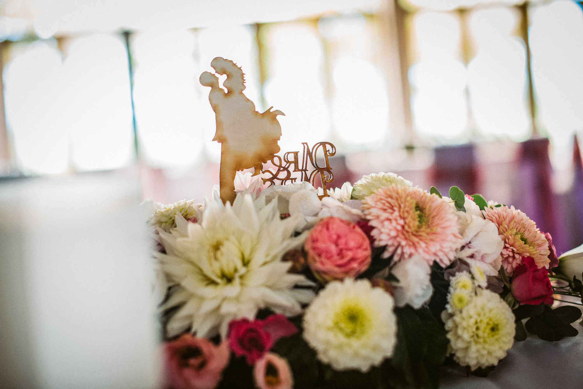 Floral centrepiece with wooden couple topper, shallow depth of field detail.