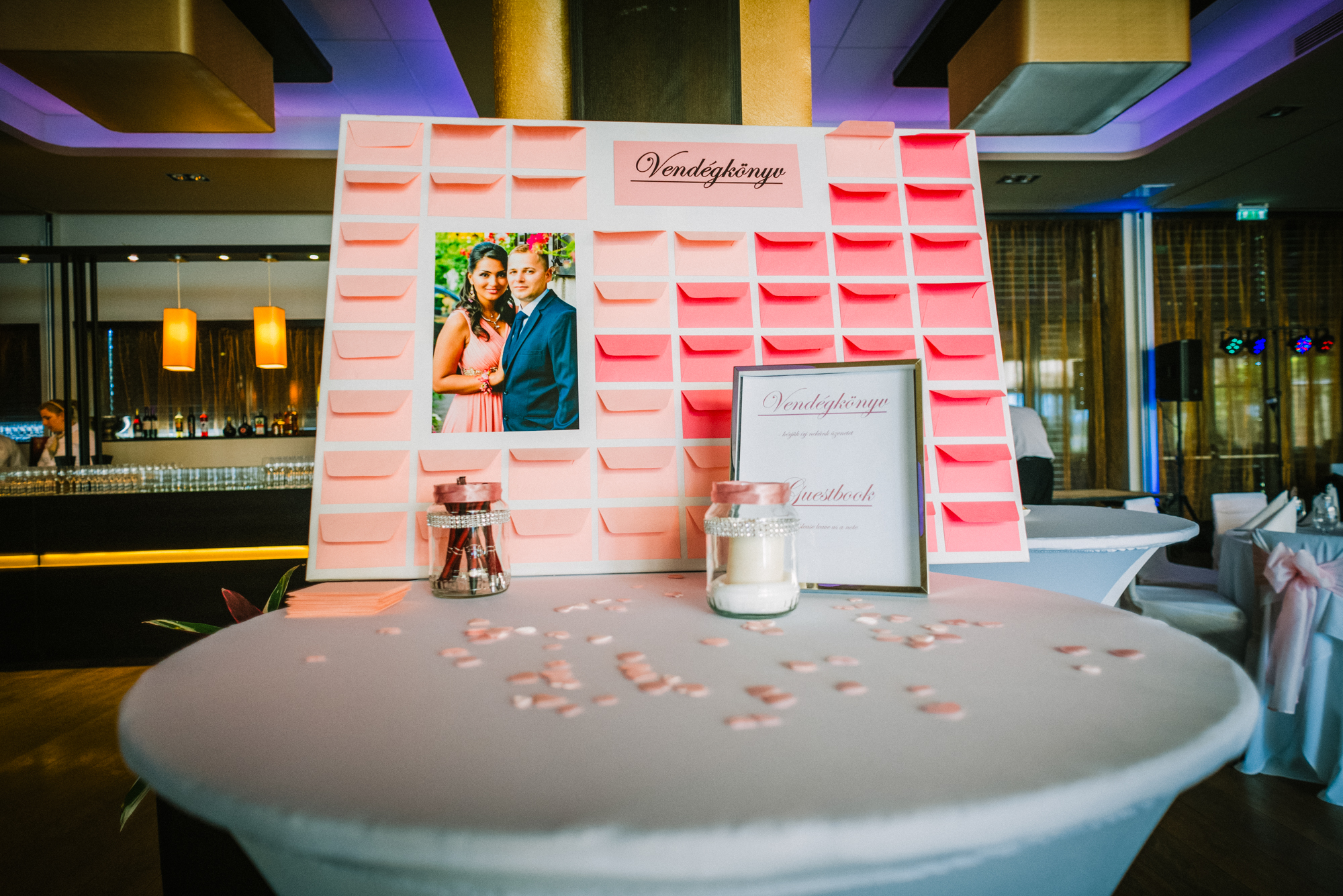 Wedding guestbook table with pink notes and couple portrait, modern reception detail.