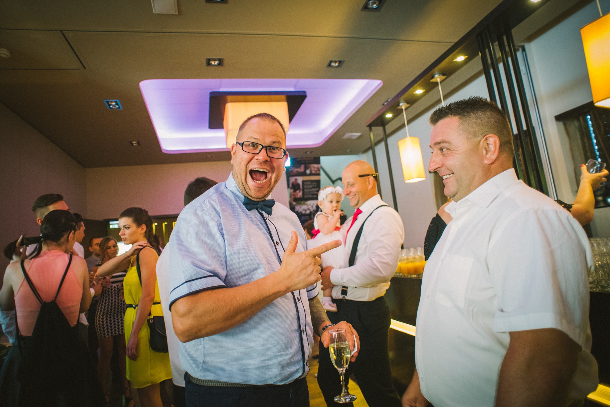 Guests laughing and holding drinks during wedding reception, lively candid moment.