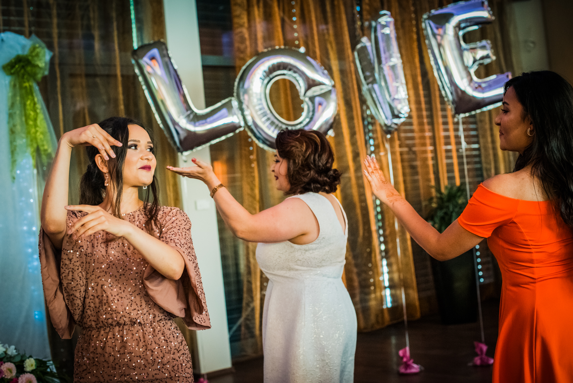 Guests dancing in front of silver love balloons, colourful wedding party scene.