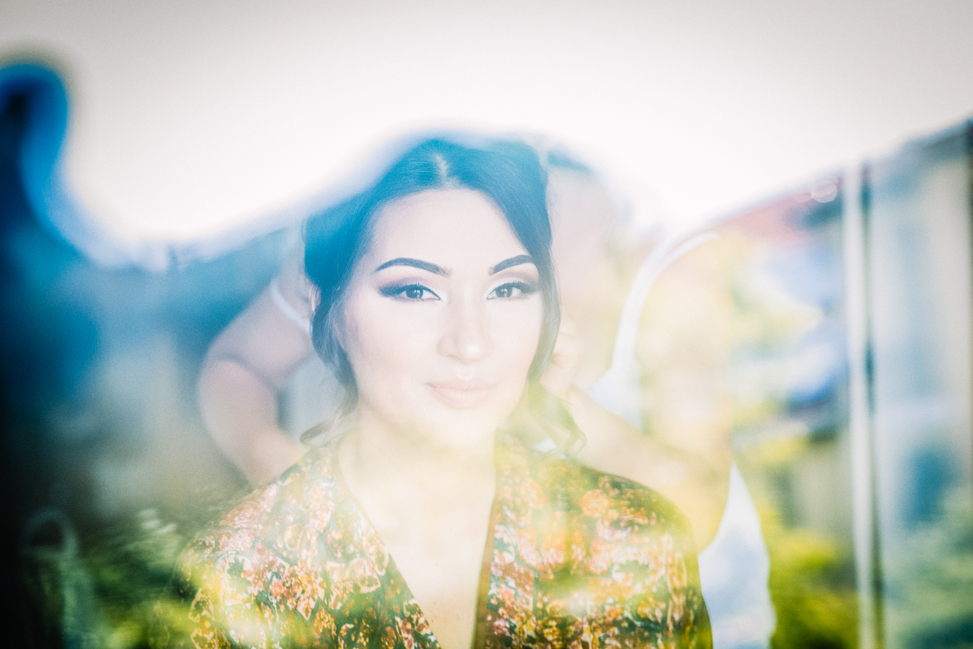 Bride reflection through glass during hair styling, dreamy layered composition indoors.