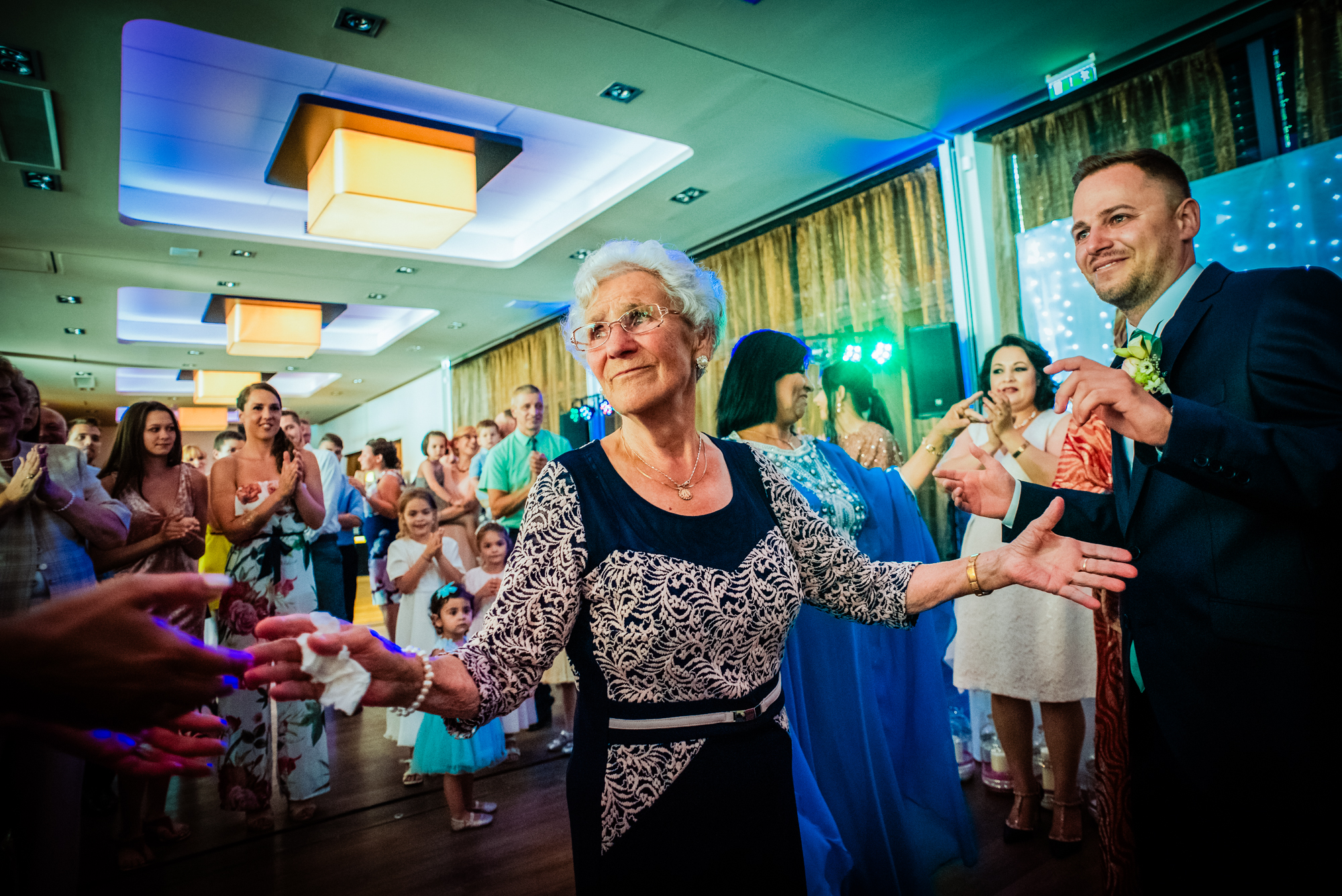 Elderly woman dancing confidently in centre of crowd, expressive celebration moment.