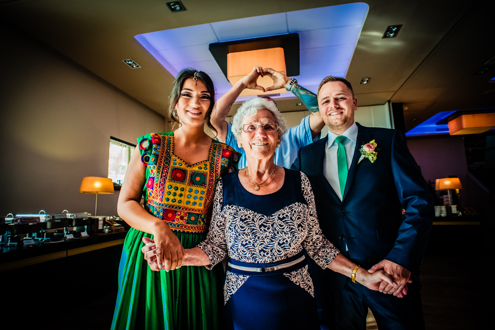 Bride, groom and elderly woman posing together indoors, joyful family portrait.