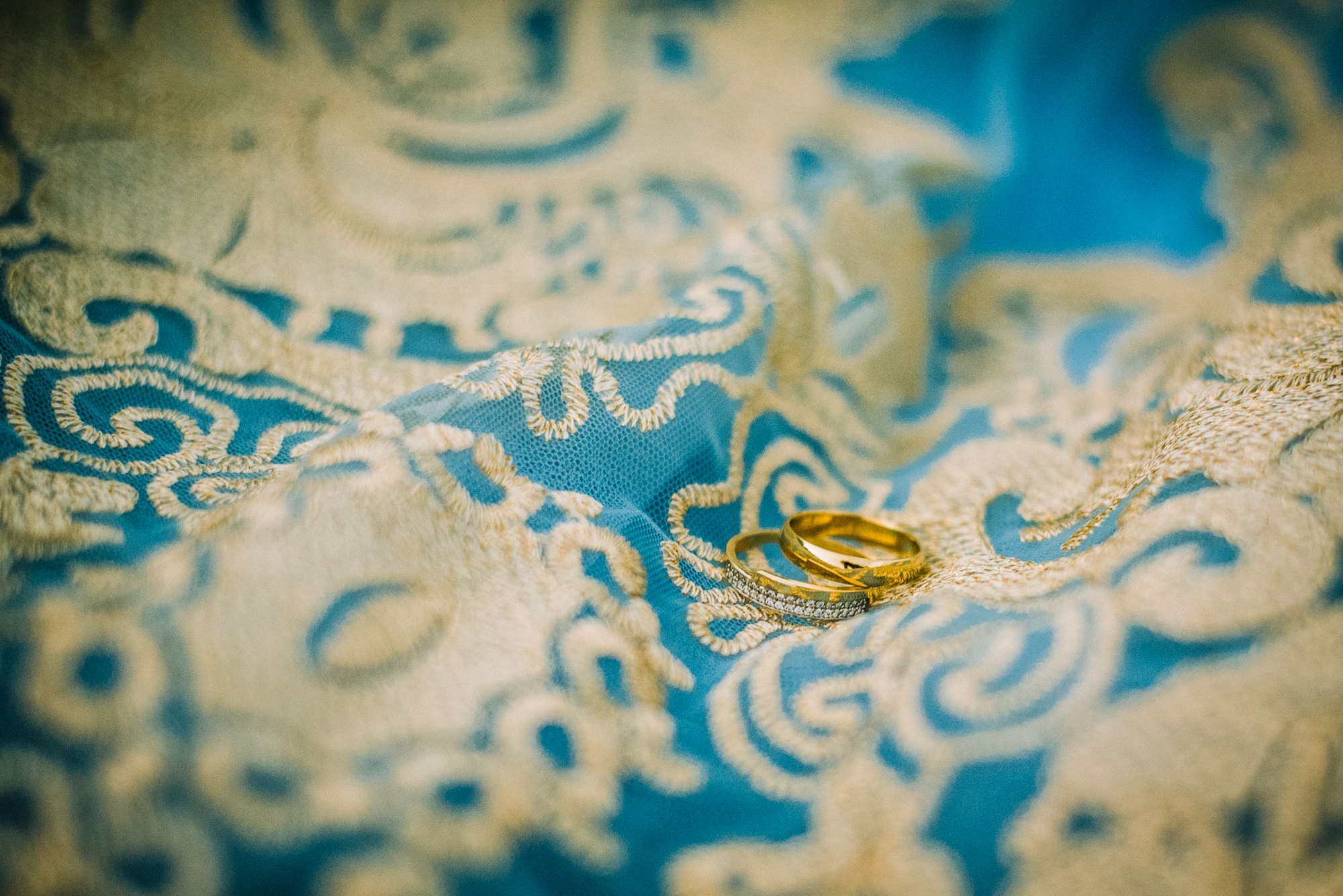 Wedding rings resting on embroidered fabric, detailed macro shot with soft textures.