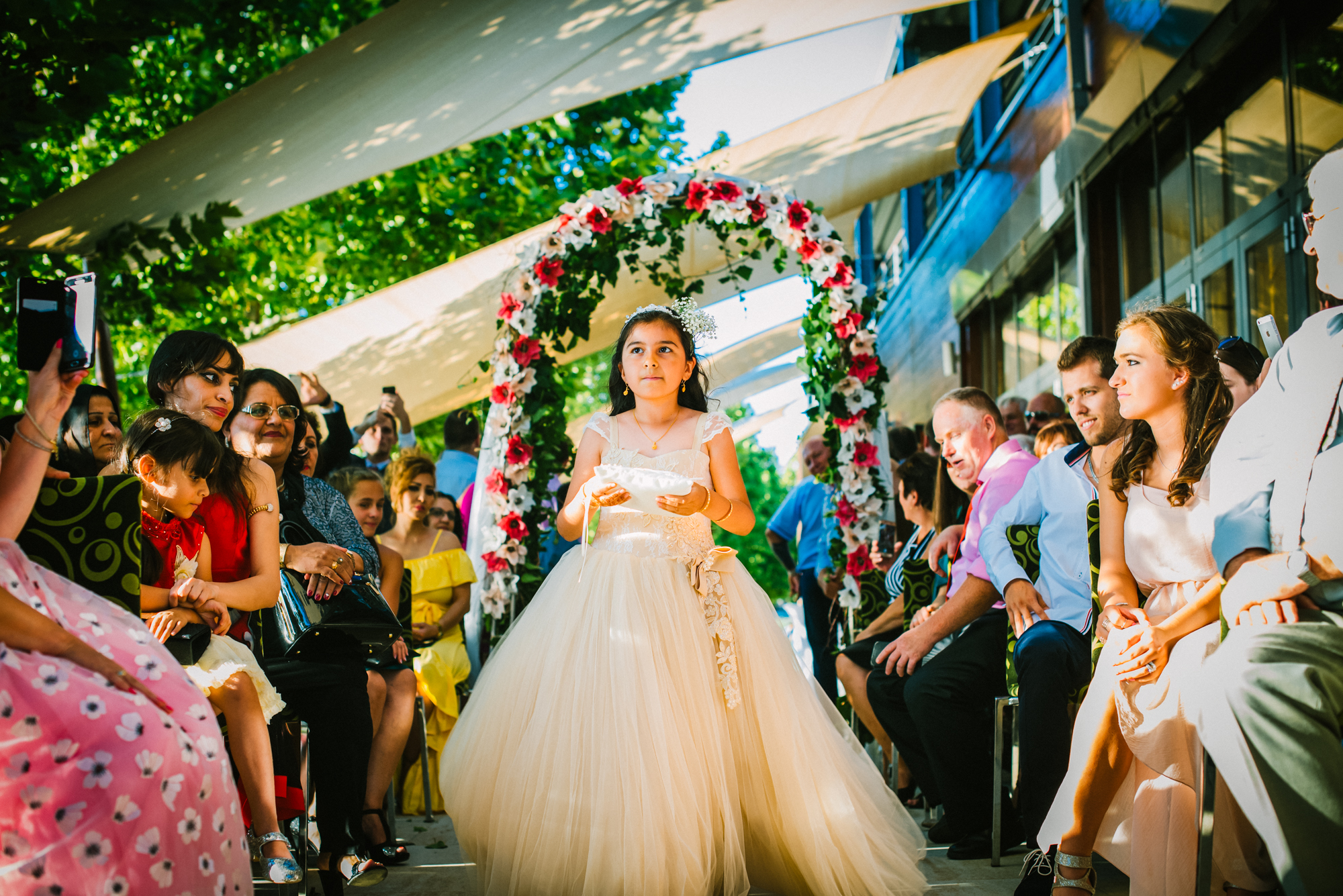 Flower girl walking down aisle under floral arch at Öbölház Budapest wedding ceremony.