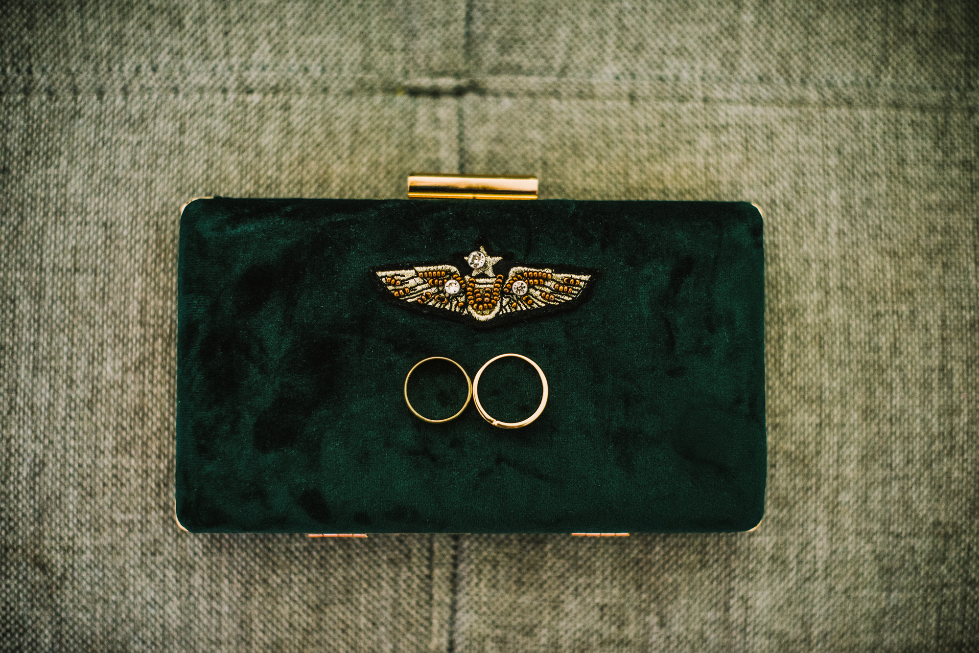 Gold wedding rings placed on green velvet clutch, elegant flat lay composition.