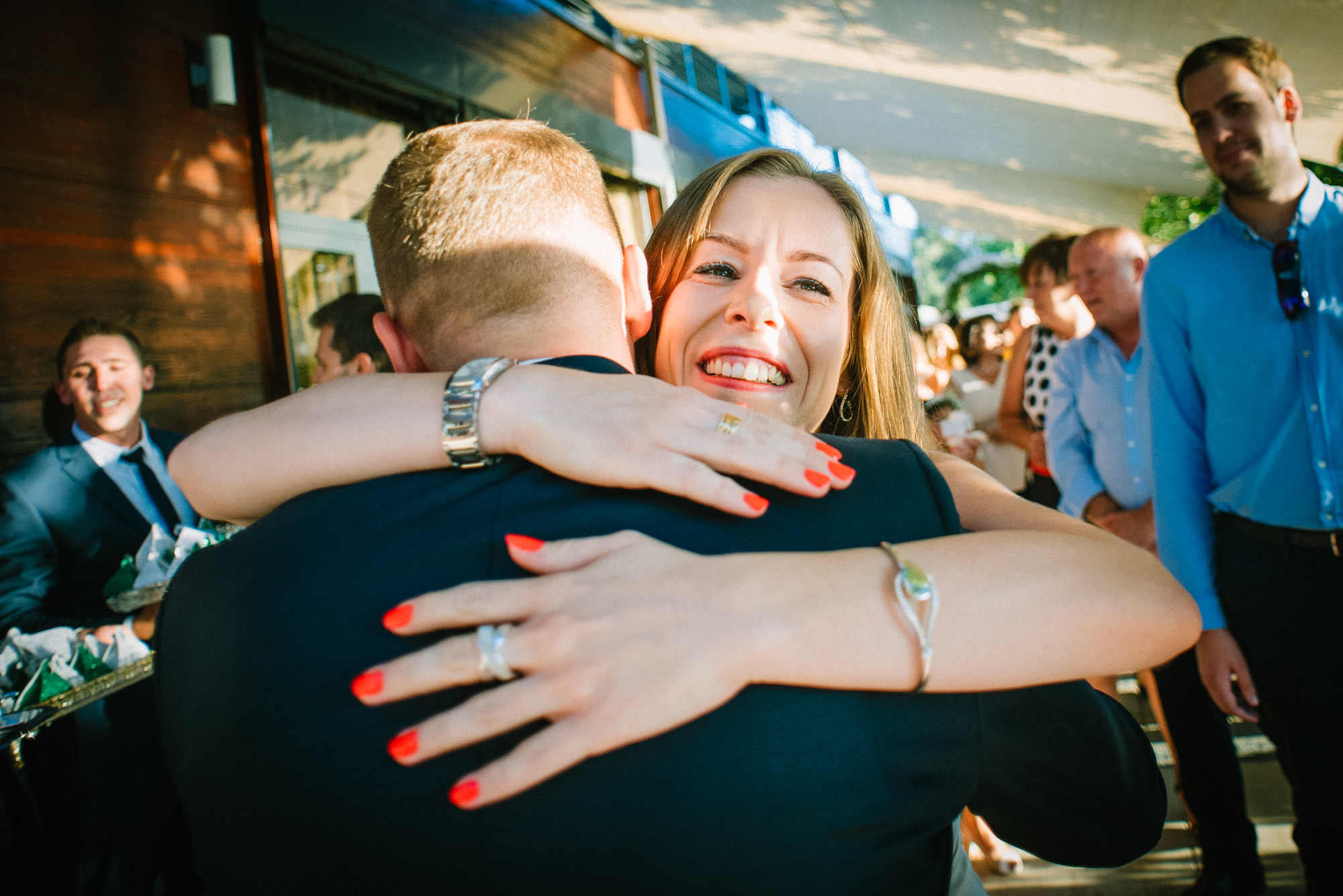 Bride hugging guest tightly during joyful wedding reception moment outdoors.