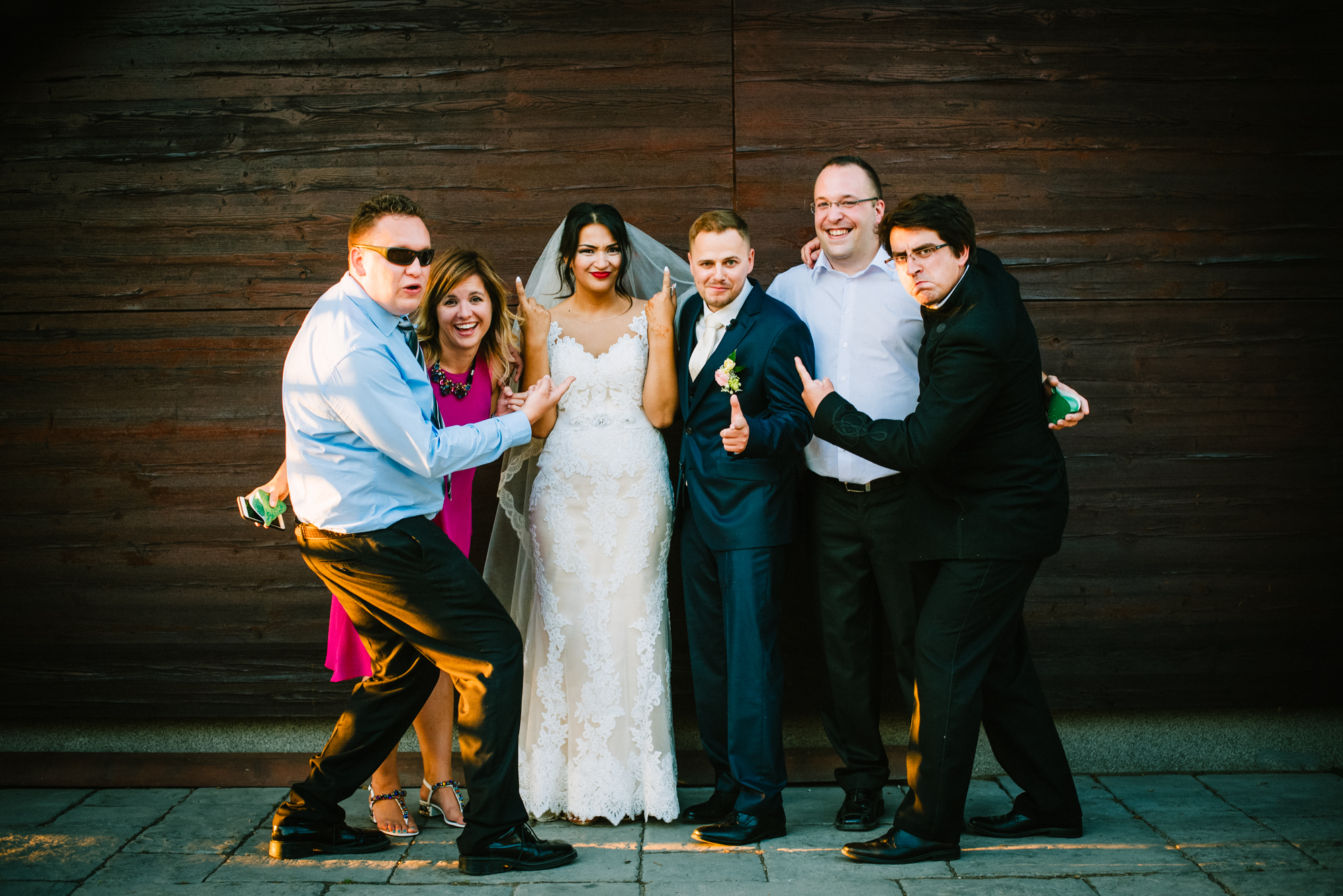 Bride and groom surrounded by friends making playful gestures during fun wedding portrait.