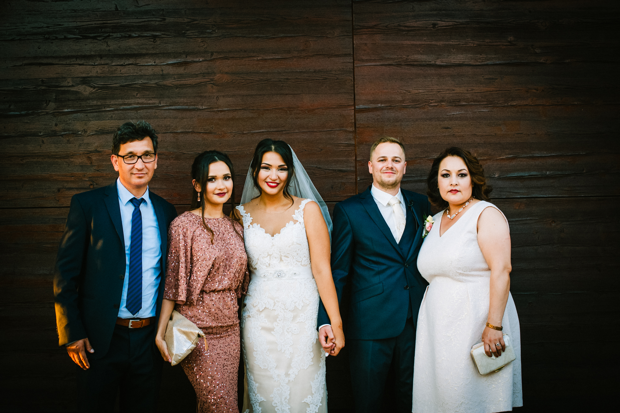 Bride and groom standing with close family members in relaxed wedding group photo.