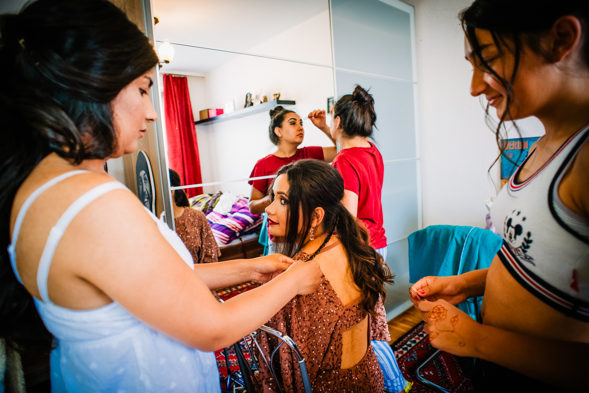Bride getting ready with friends helping dress, candid moment in Budapest apartment.