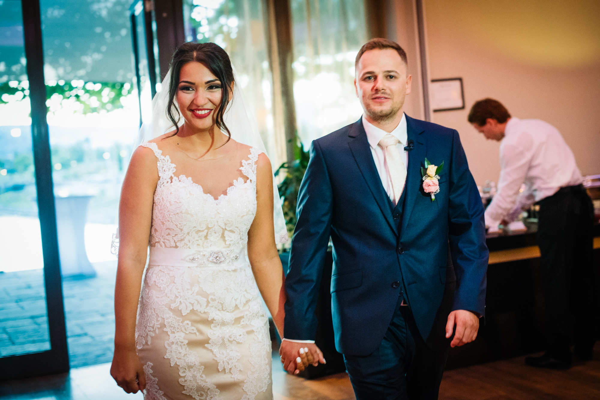 Bride and groom walking hand in hand into reception space during wedding evening.