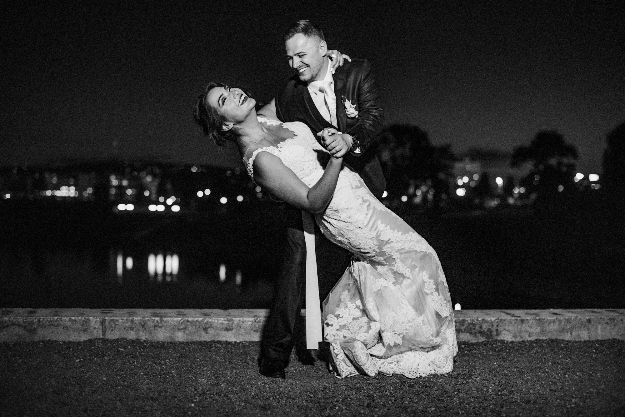 Bride and groom dancing together outdoors at night overlooking city lights.