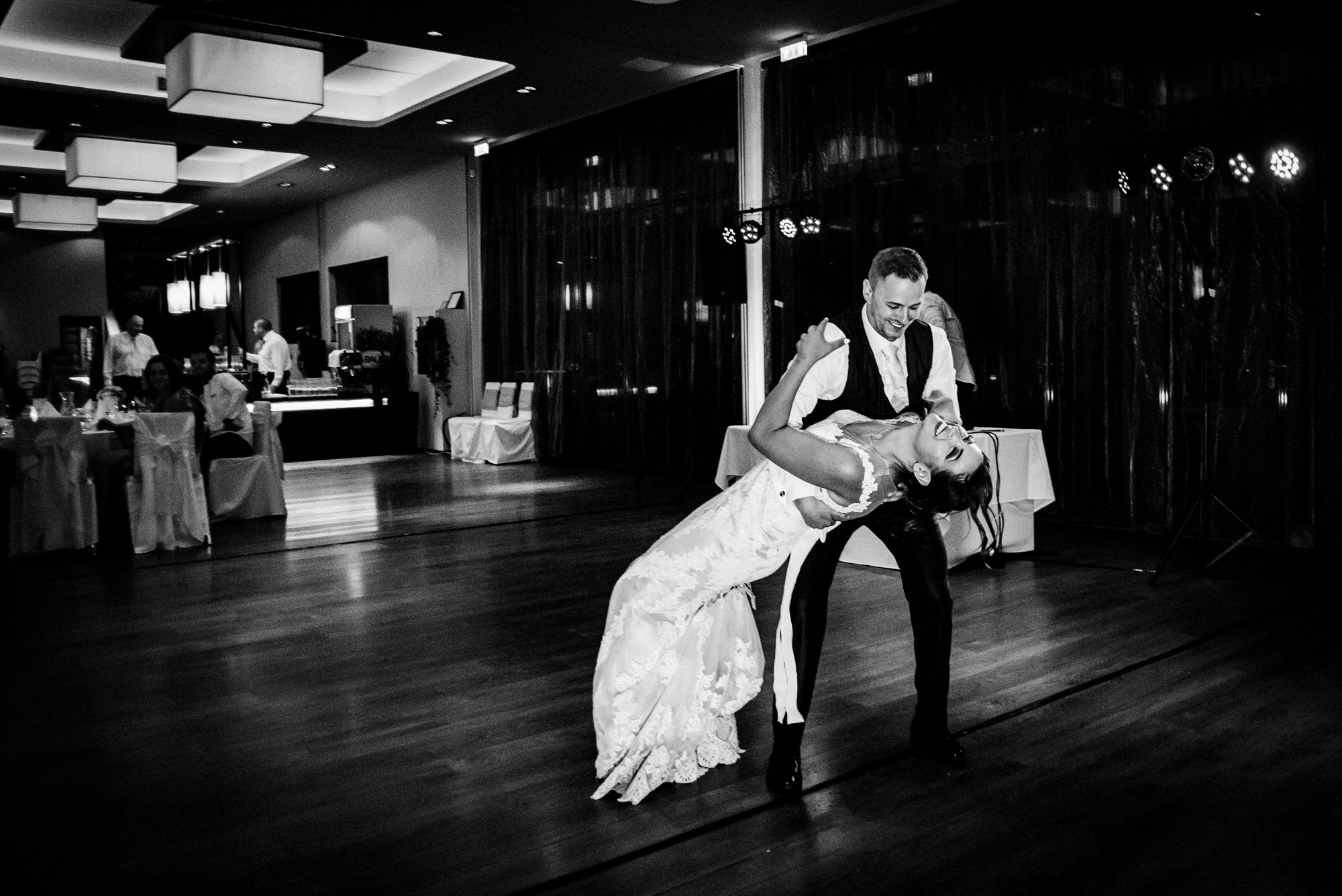 Bride dipped by groom on dance floor during evening wedding reception.