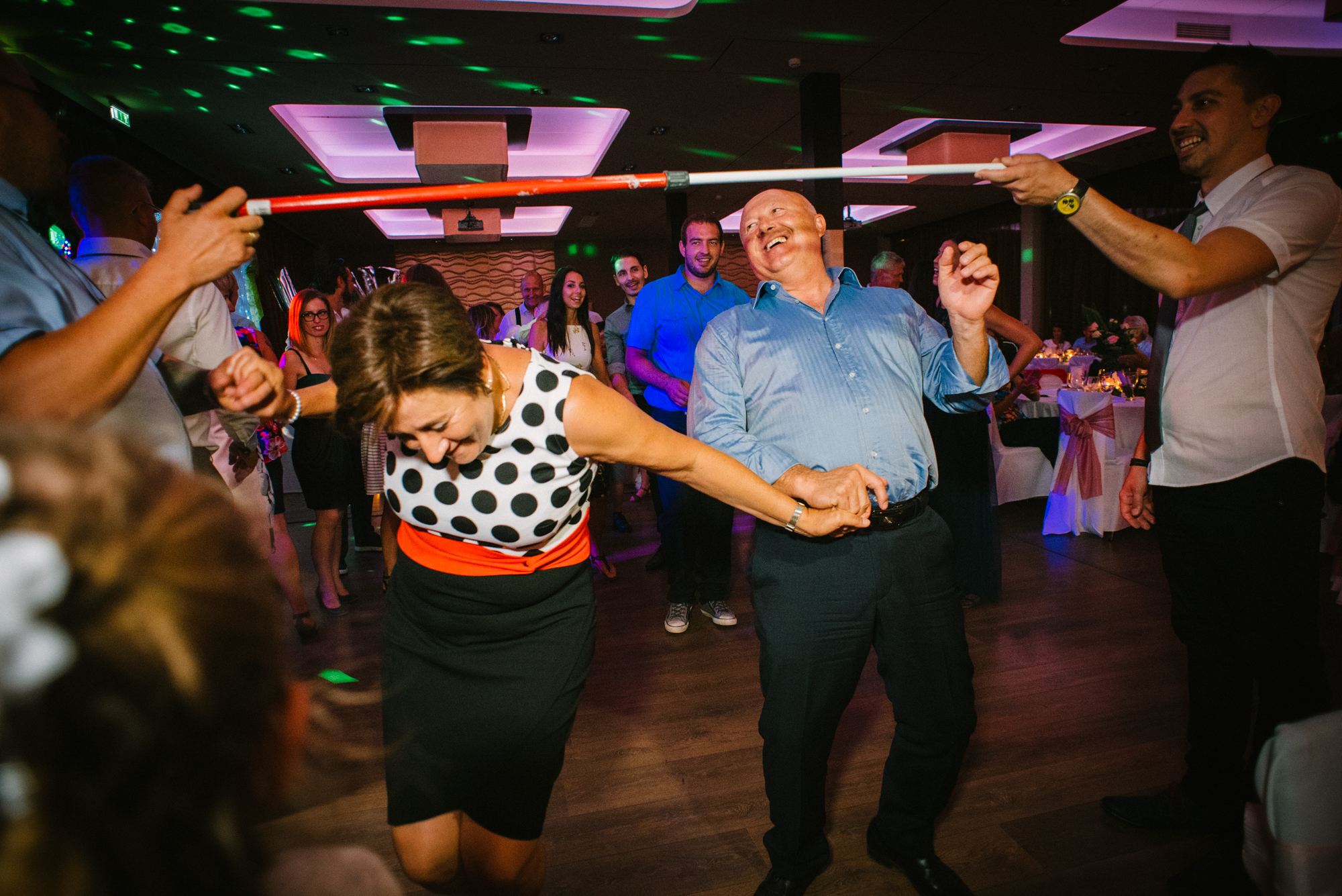 Guests dancing under limbo stick with joyful expressions and colourful lighting effects.
